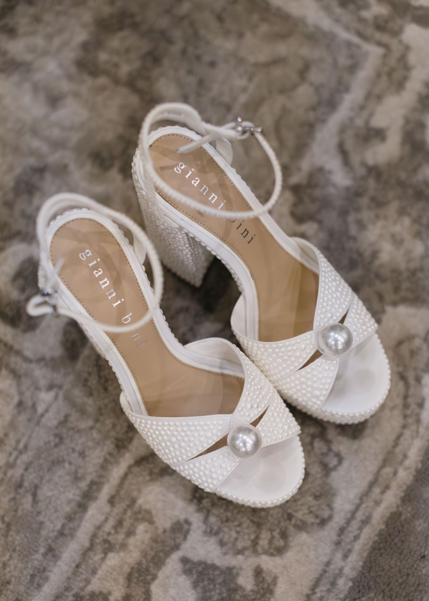 White crystal-embellished bridal sandals with ankle straps and pearl details on stone surface.