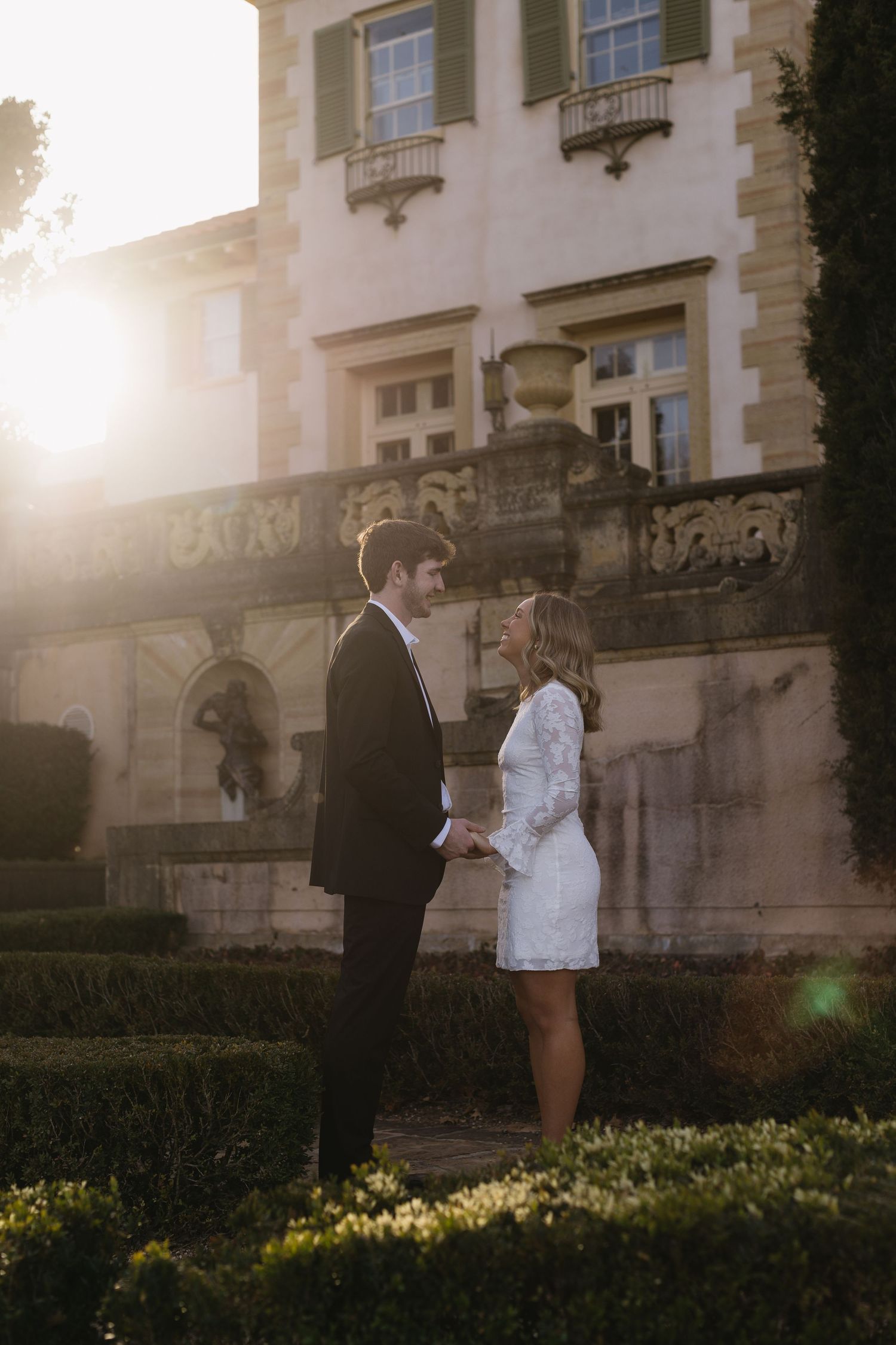 A romantic moment captured at sunset in front of a grand estate building.