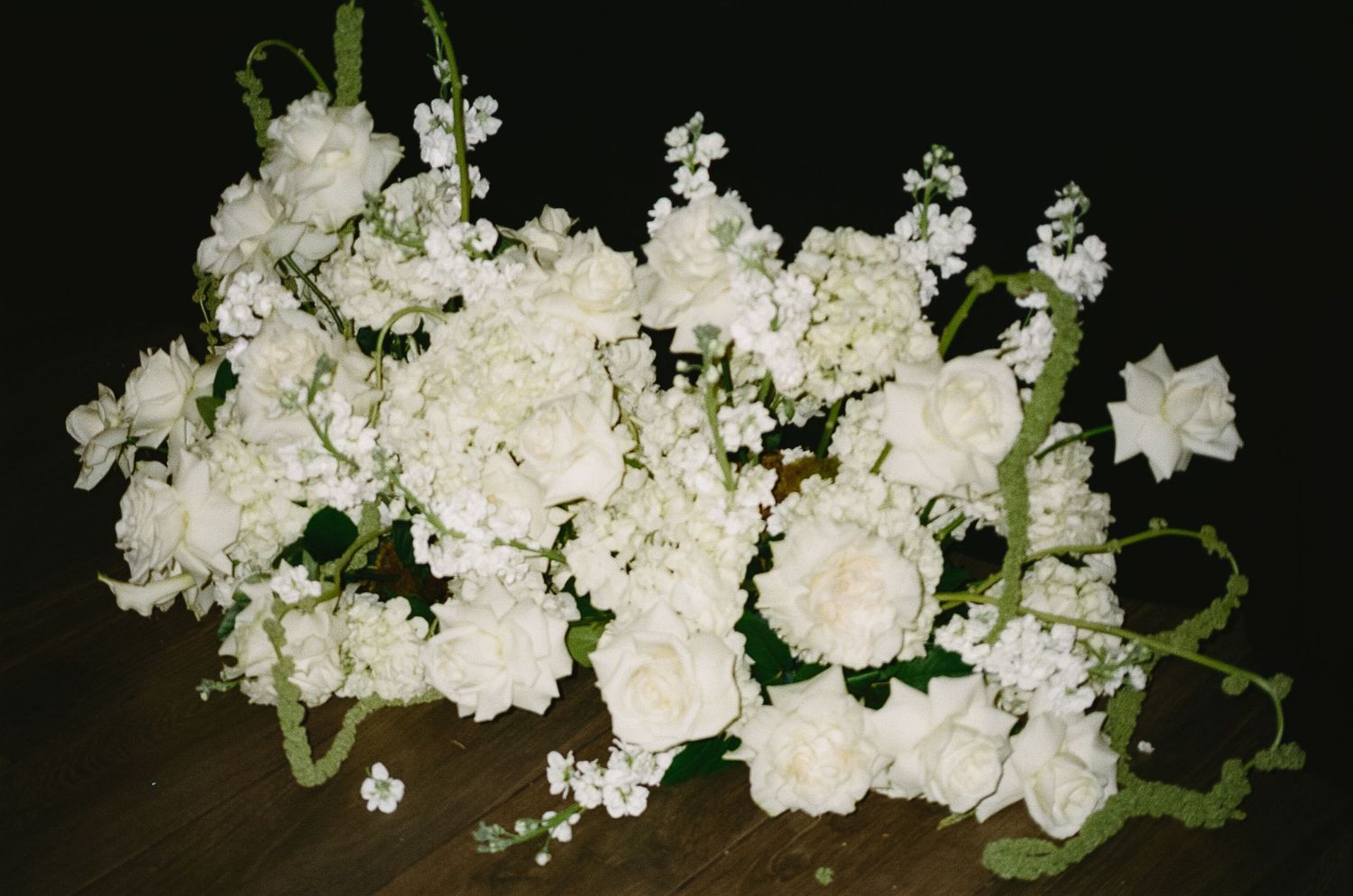White floral arrangement featuring roses and hydrangeas against dark background.