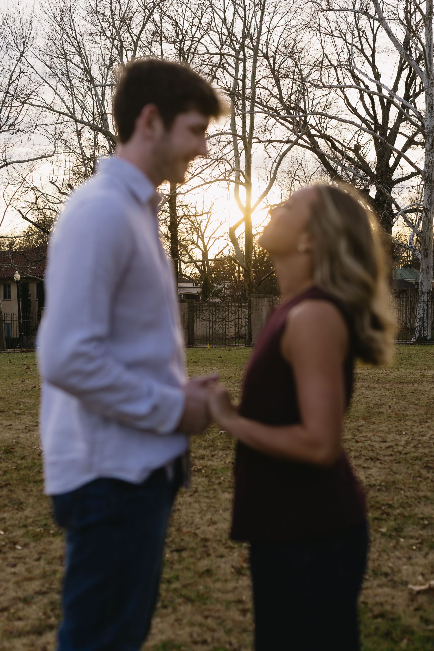 Silhouetted couple standing together at sunset with bare trees in background.