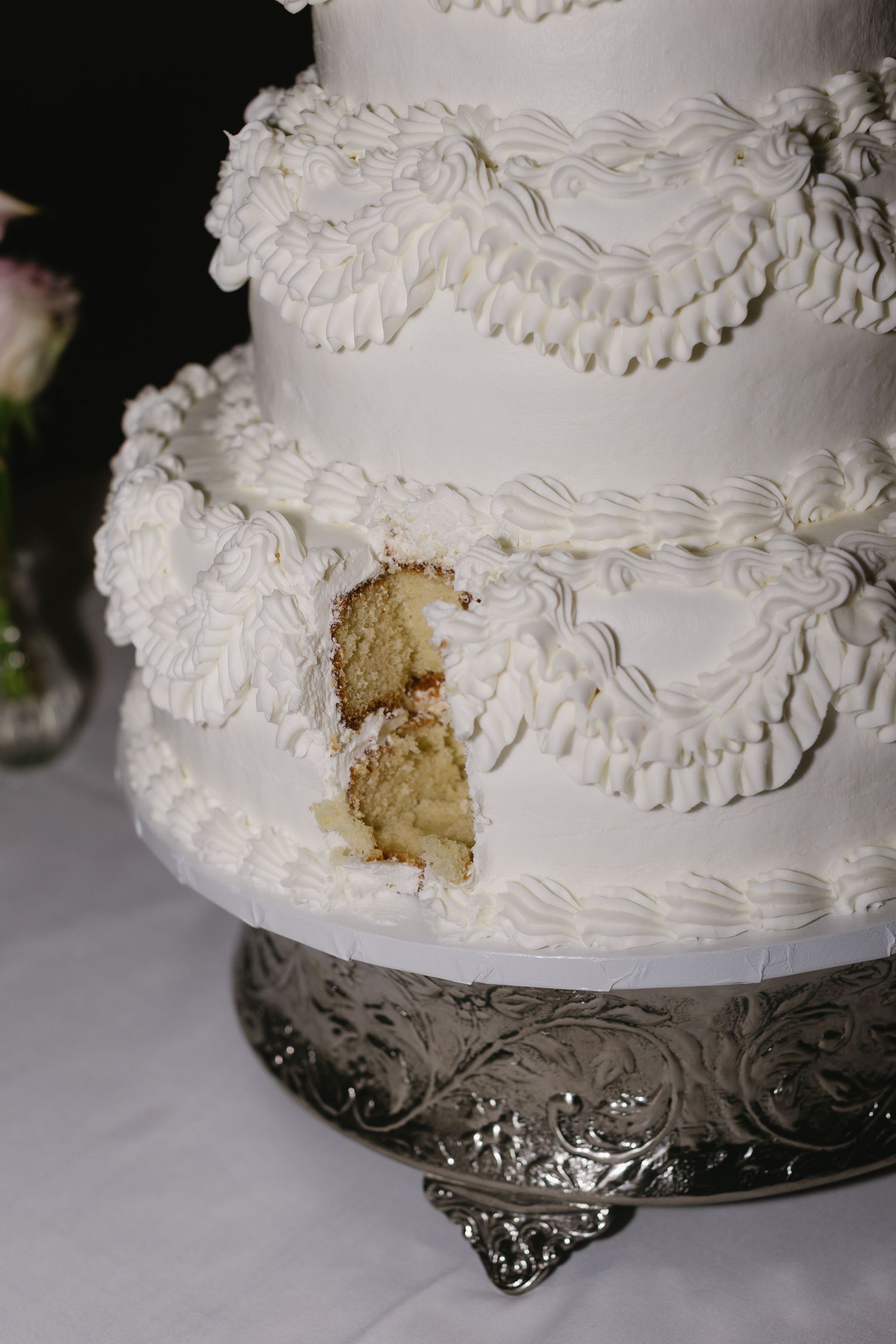 White wedding cake with decorative piping and a slice removed on silver cake stand.
