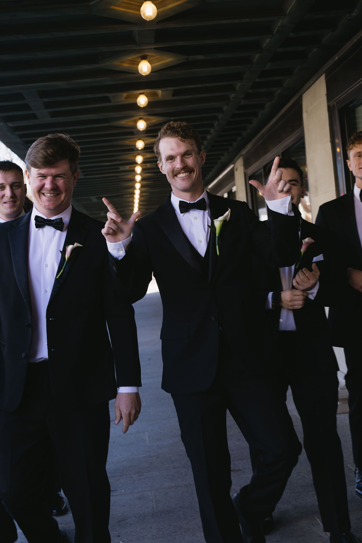Groomsmen laughing and posing casually in black tuxedos.