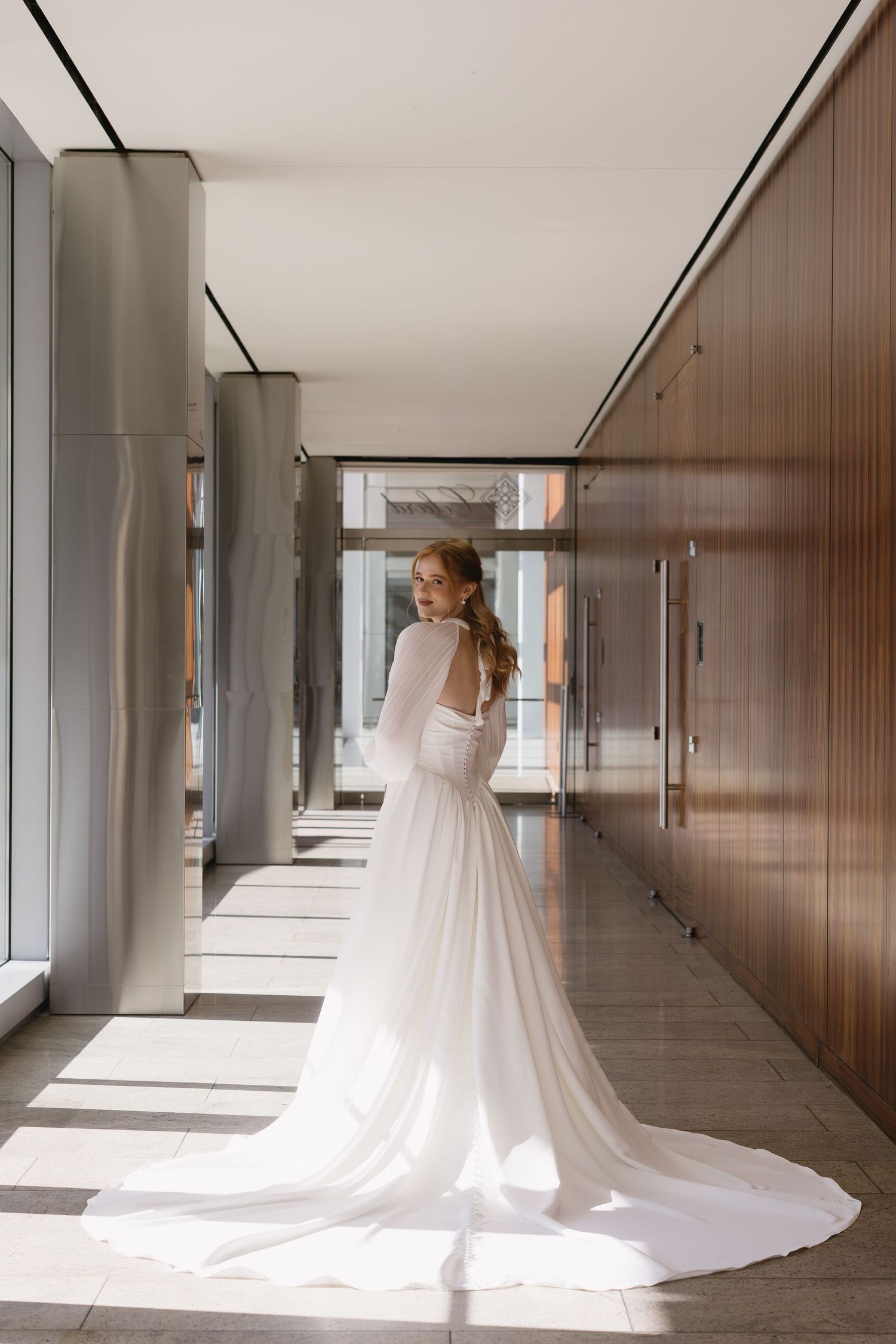 Stunning bridal gown with long train photographed in a modern hallway with natural light.