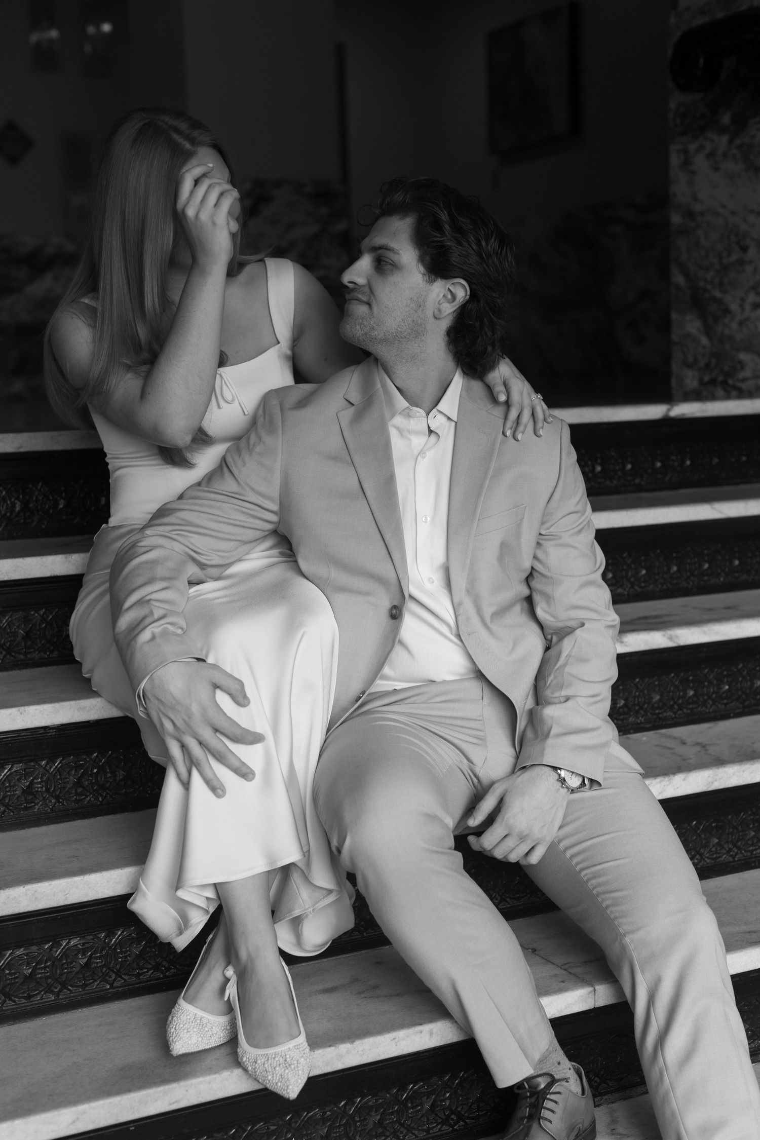 A couple in matching light colors sits together on steps in black and white photography.