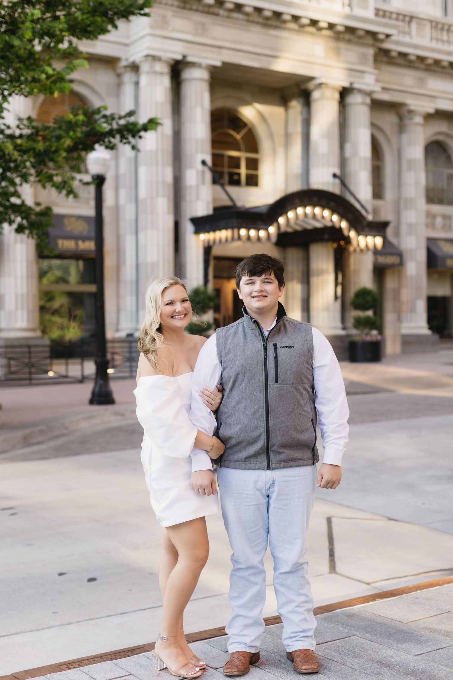 A couple poses together in formal attire on stone steps outside a grand building with classic architecture.