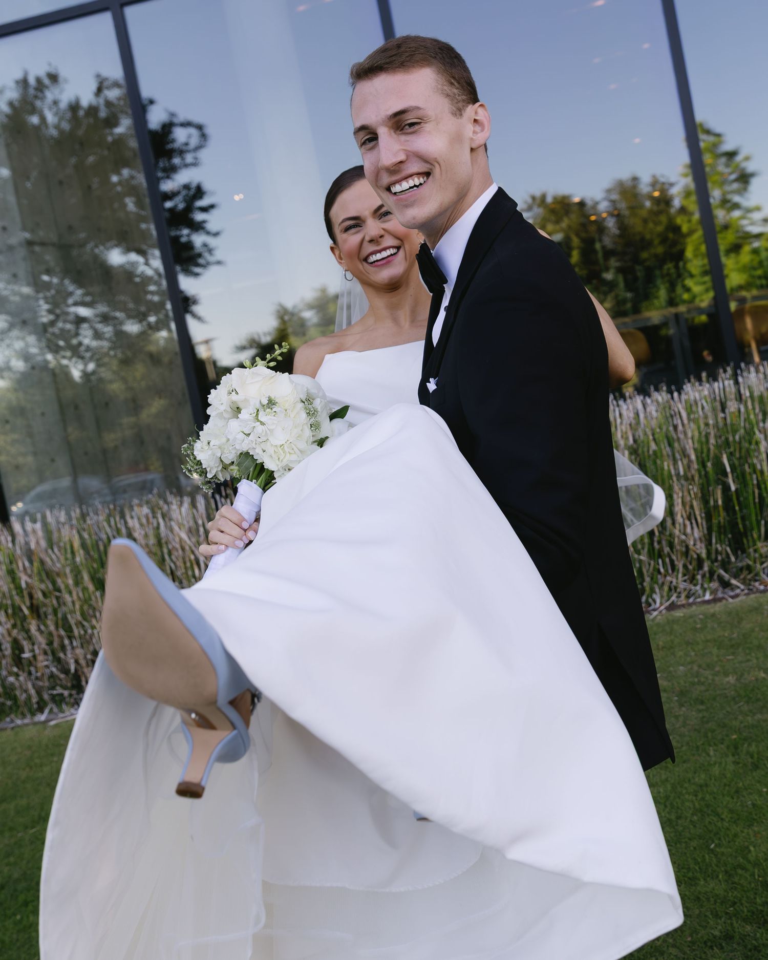 Joyful couple in wedding attire walking and laughing together in a garden setting.