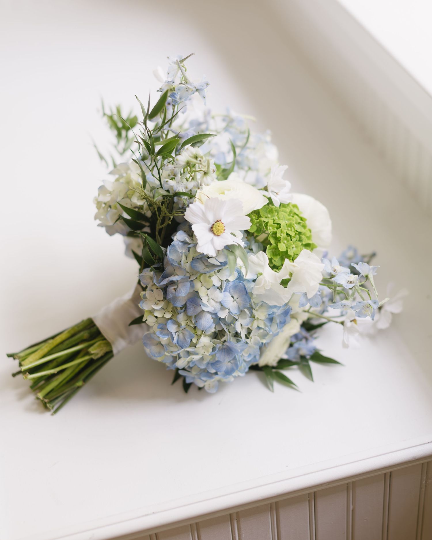 A wedding bouquet with white and pale blue hydrangeas arranged on a light-colored surface.