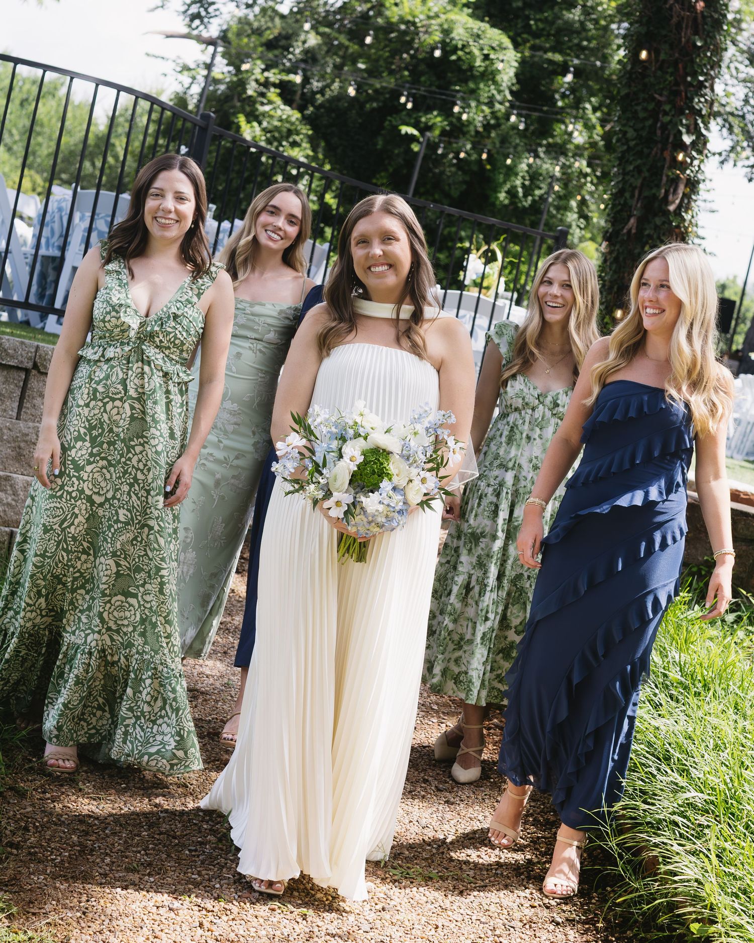 Bridesmaids in navy and floral dresses posing outdoors with the bride in white.