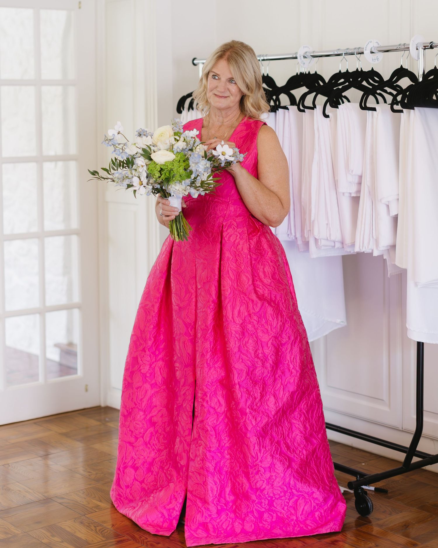 A person wearing a vibrant hot pink formal gown holding a bouquet of white and green flowers.