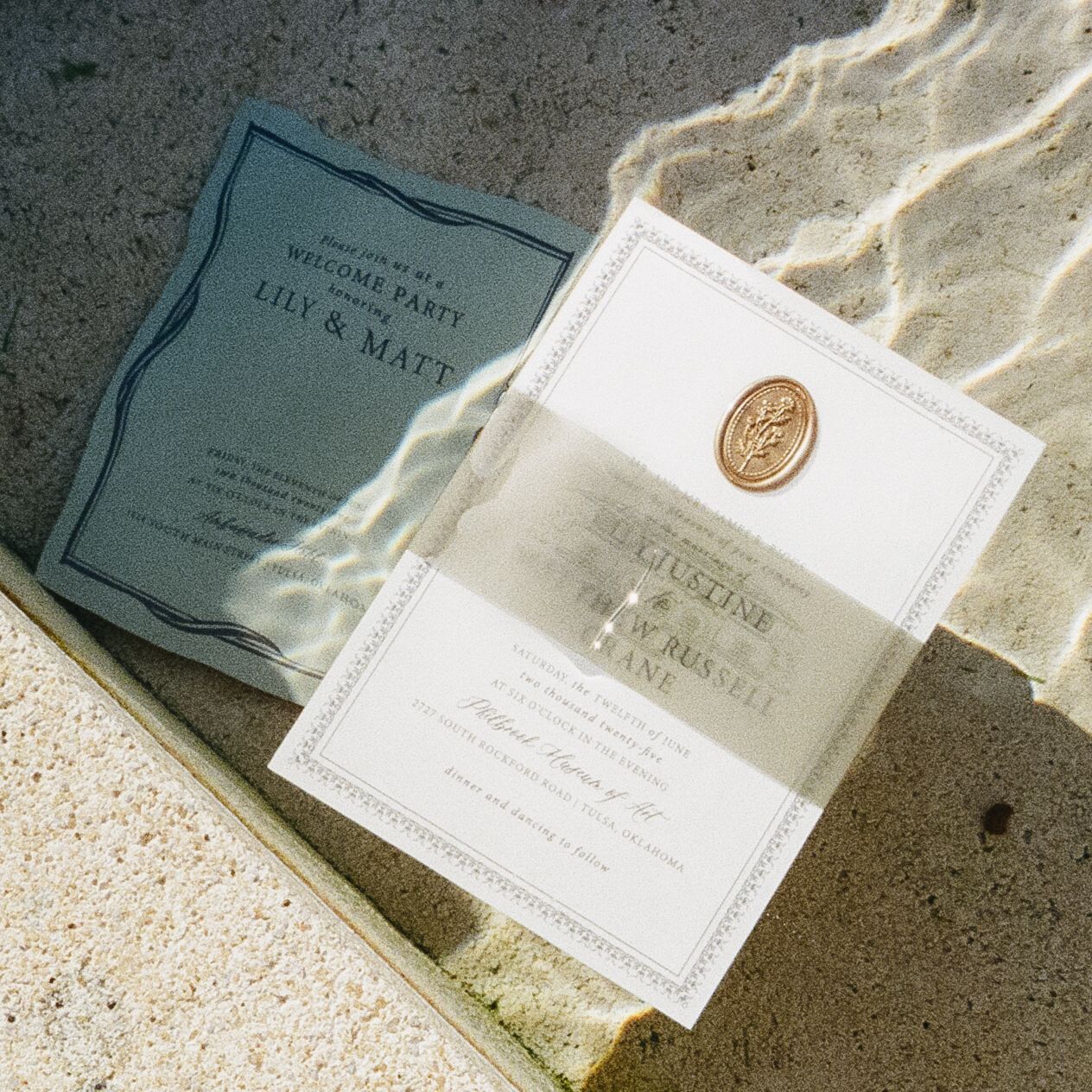 Elegant wedding invitations with wax seal photographed in natural light on concrete.