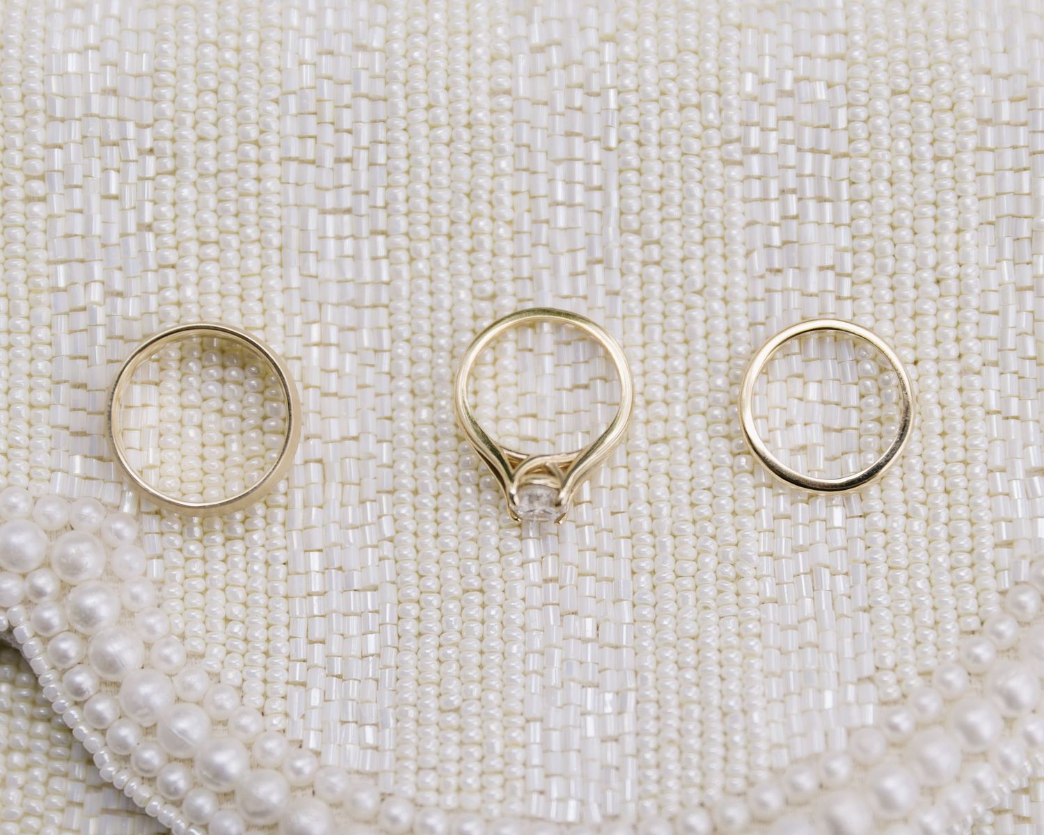 Three gold wedding rings arranged on a white beaded surface with elegant details.