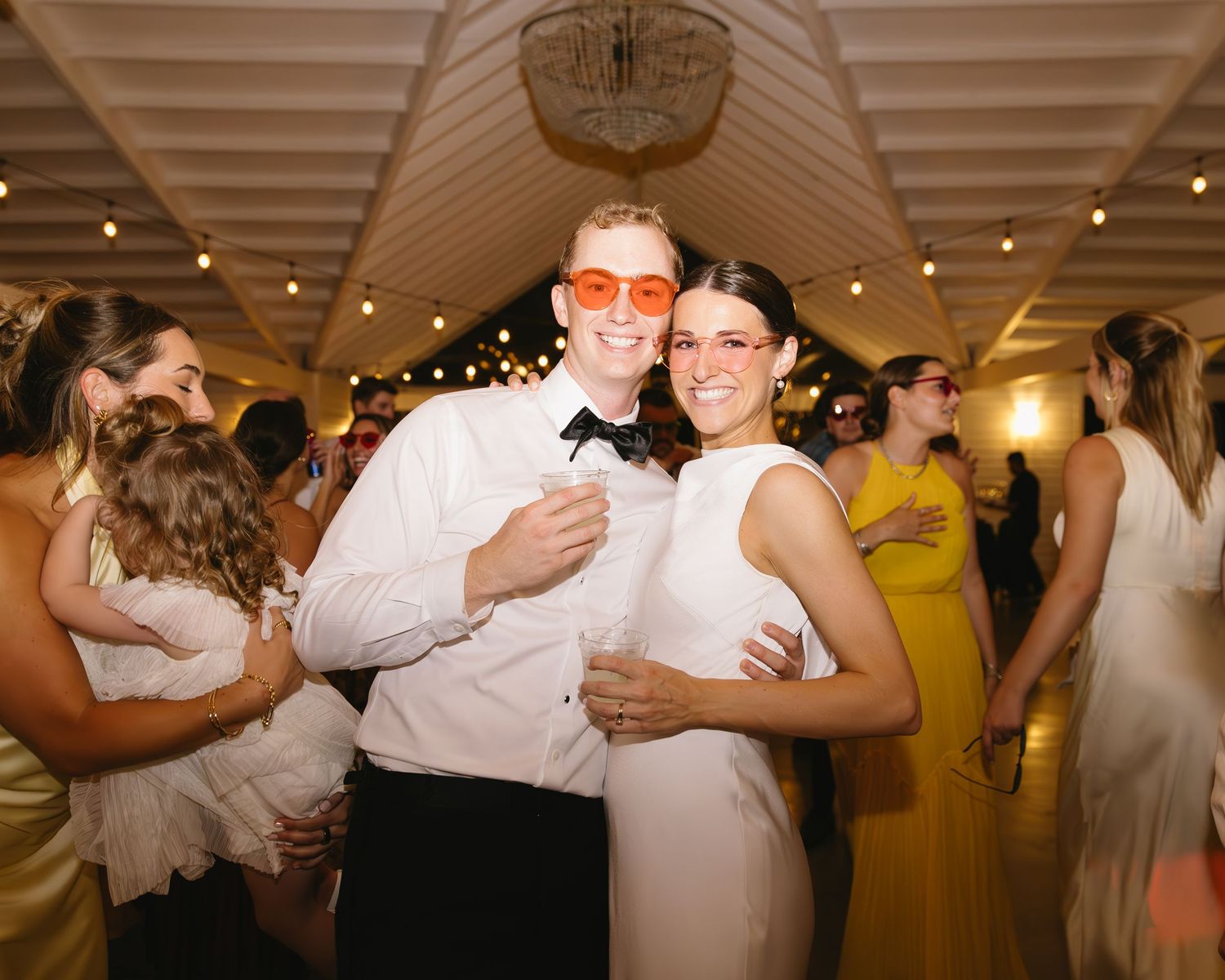 Wedding reception with string lights overhead as couples dance and celebrate on the dance floor.