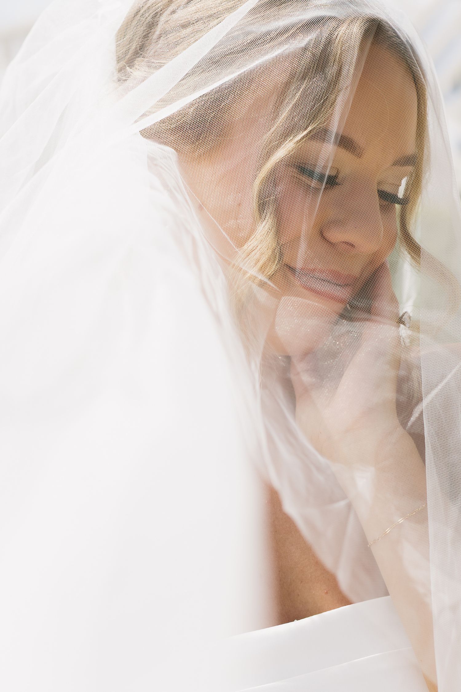 Soft, ethereal bridal portrait through delicate white veil creating a dreamy effect.
