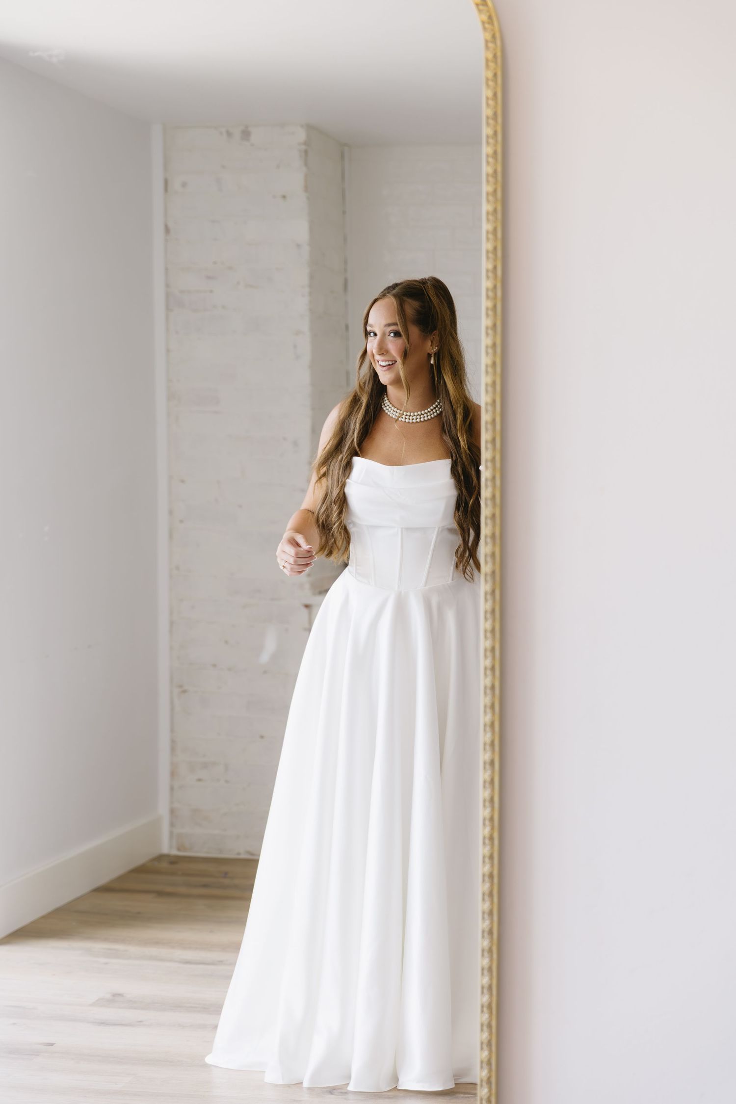 Young person wearing a white sleeveless dress poses against a light colored wall.