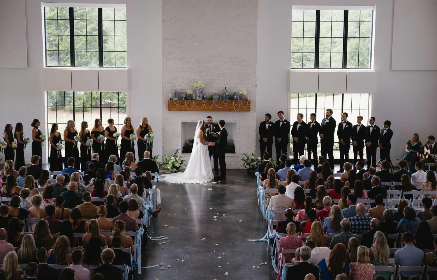 Wide view of wedding ceremony with guests seated in bright, airy venue.