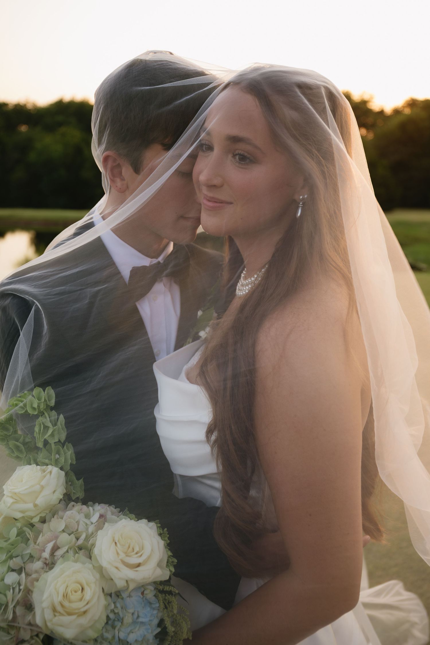 A romantic sunset wedding photo with white roses and flowing veil.
