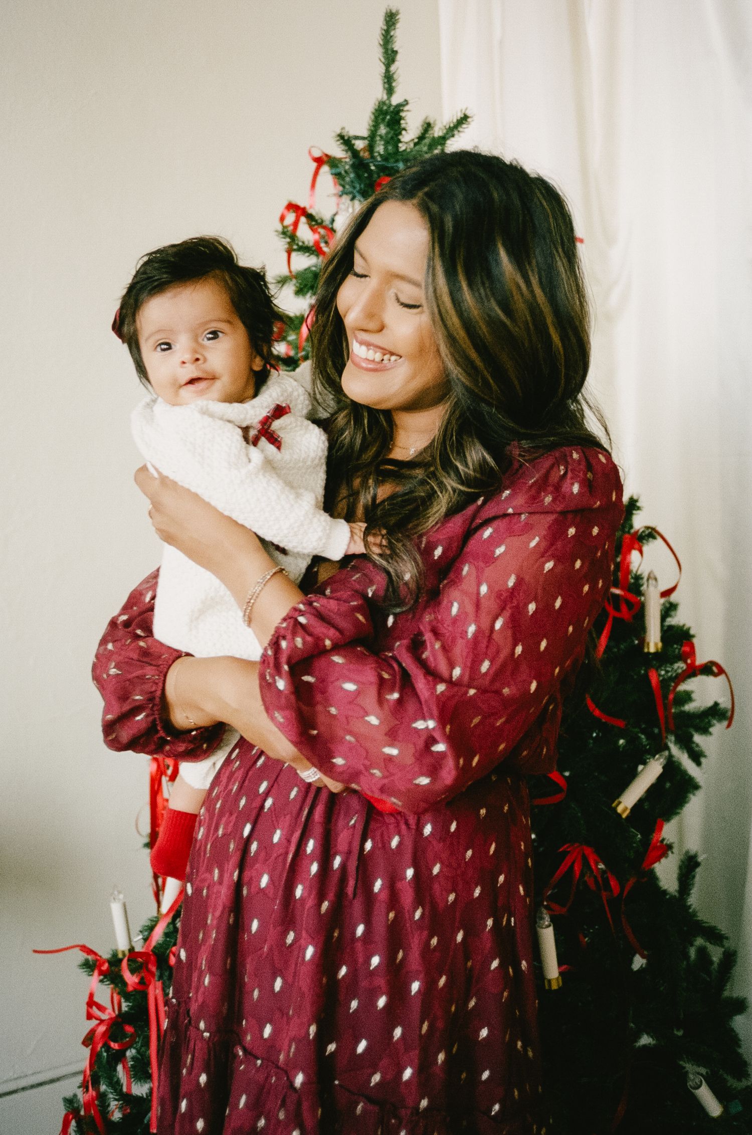 A festive holiday photoshoot with a burgundy polka dot dress and Christmas tree in the background.