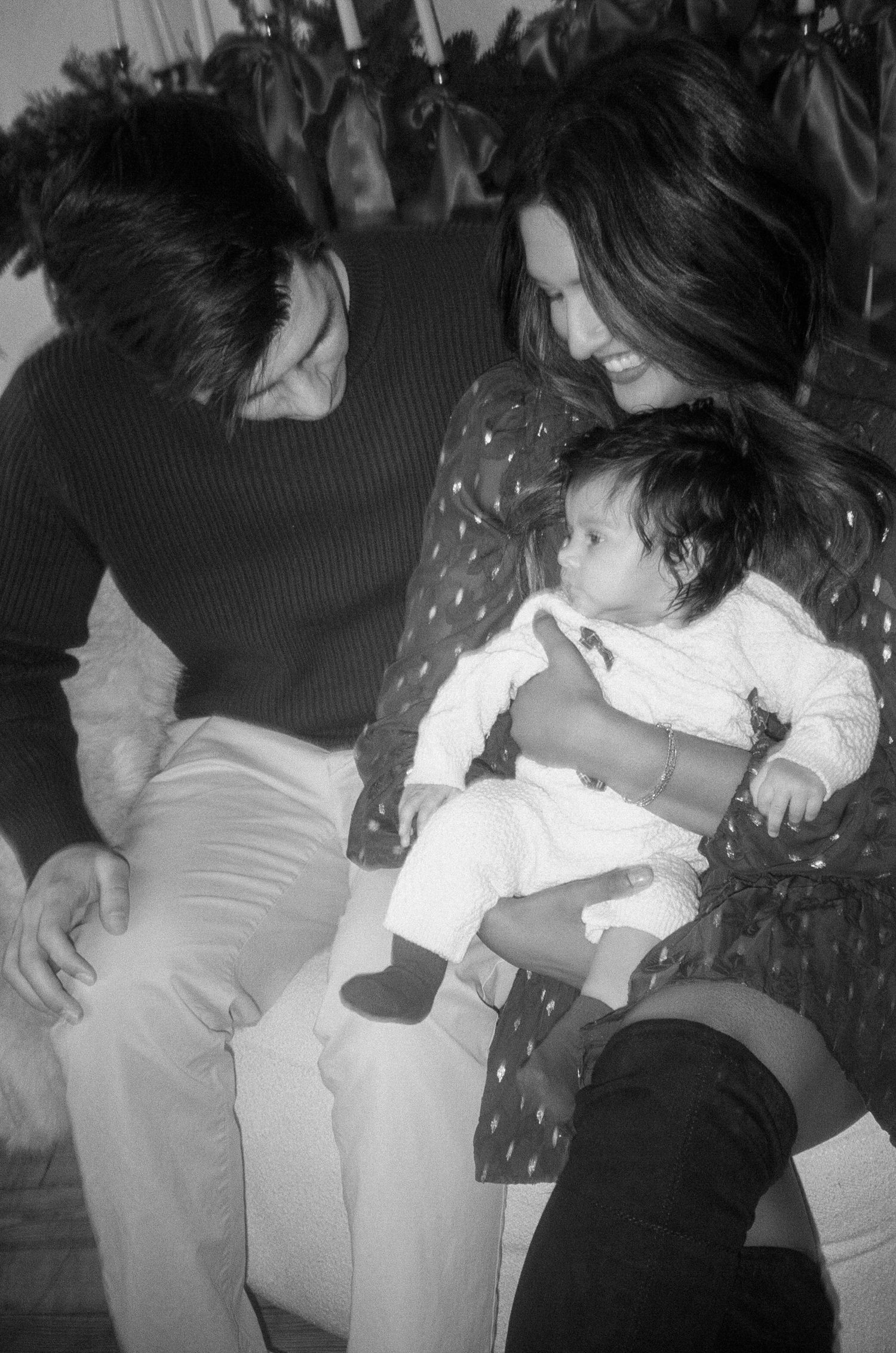A black and white photo showing a tender family moment with a baby in white clothing.