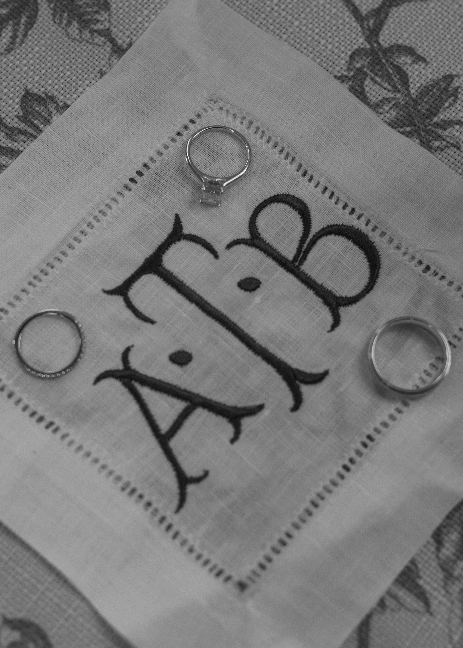 Monogrammed initials embroidered on white linen napkin with decorative border.
