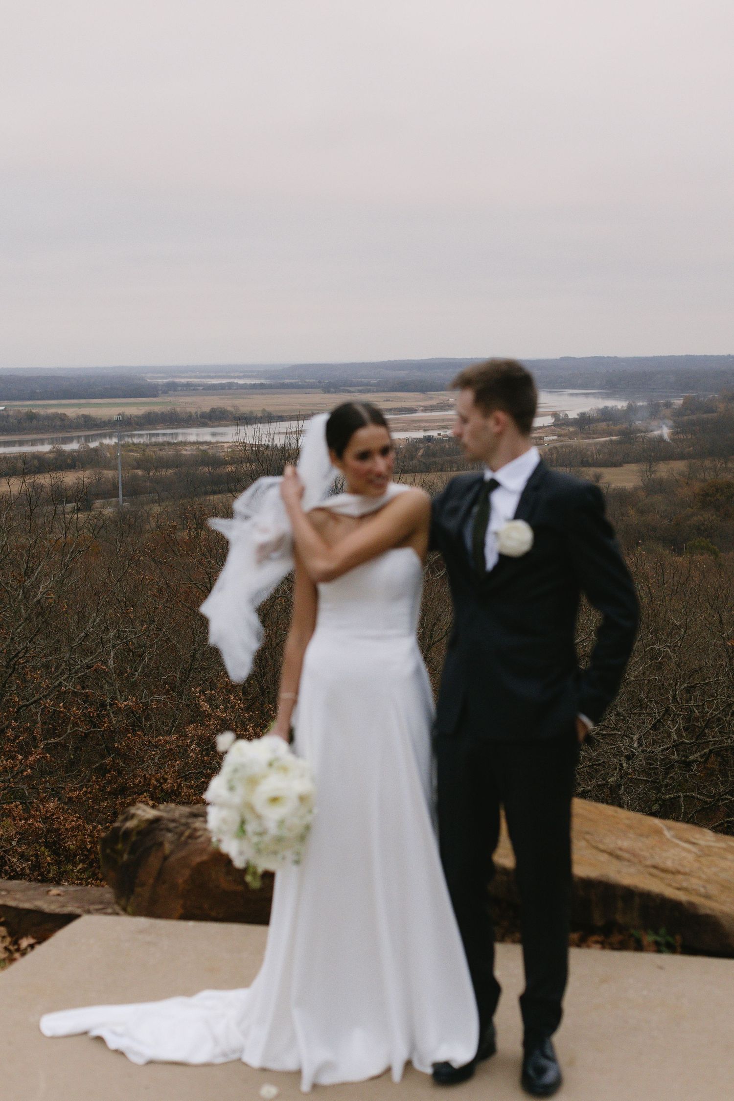 Wedding couple posing on scenic overlook with sweeping landscape view in background.