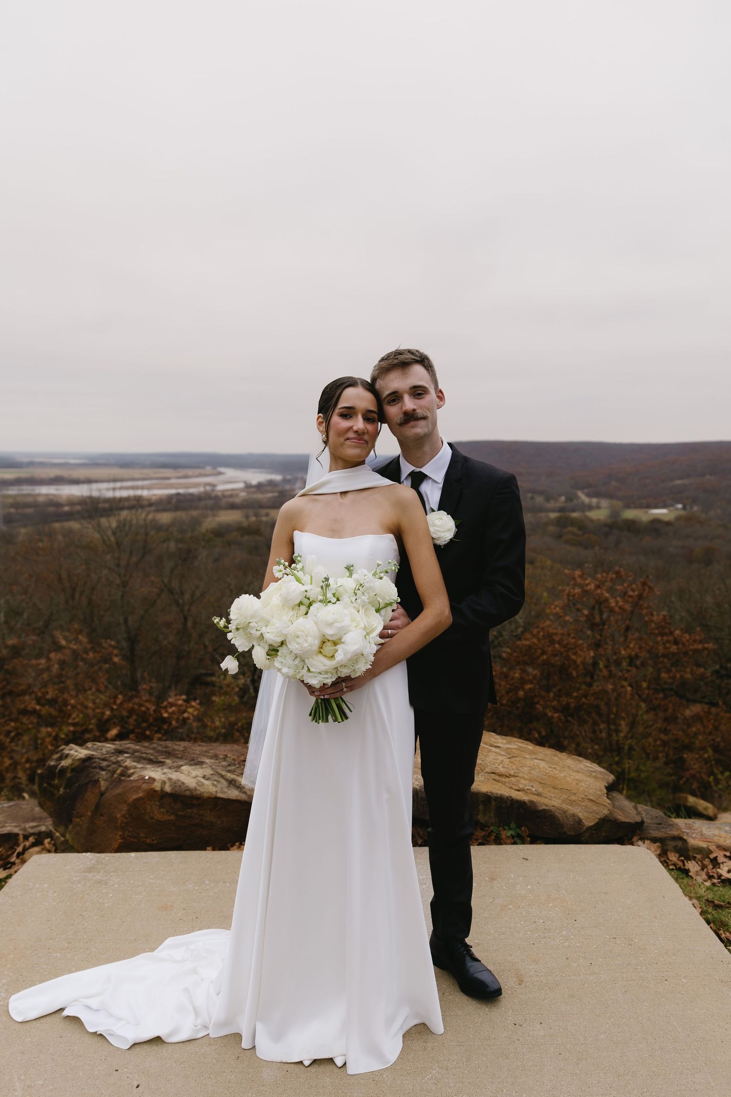 Newlyweds pose for portraits on a scenic mountain overlook with autumn foliage in the background.