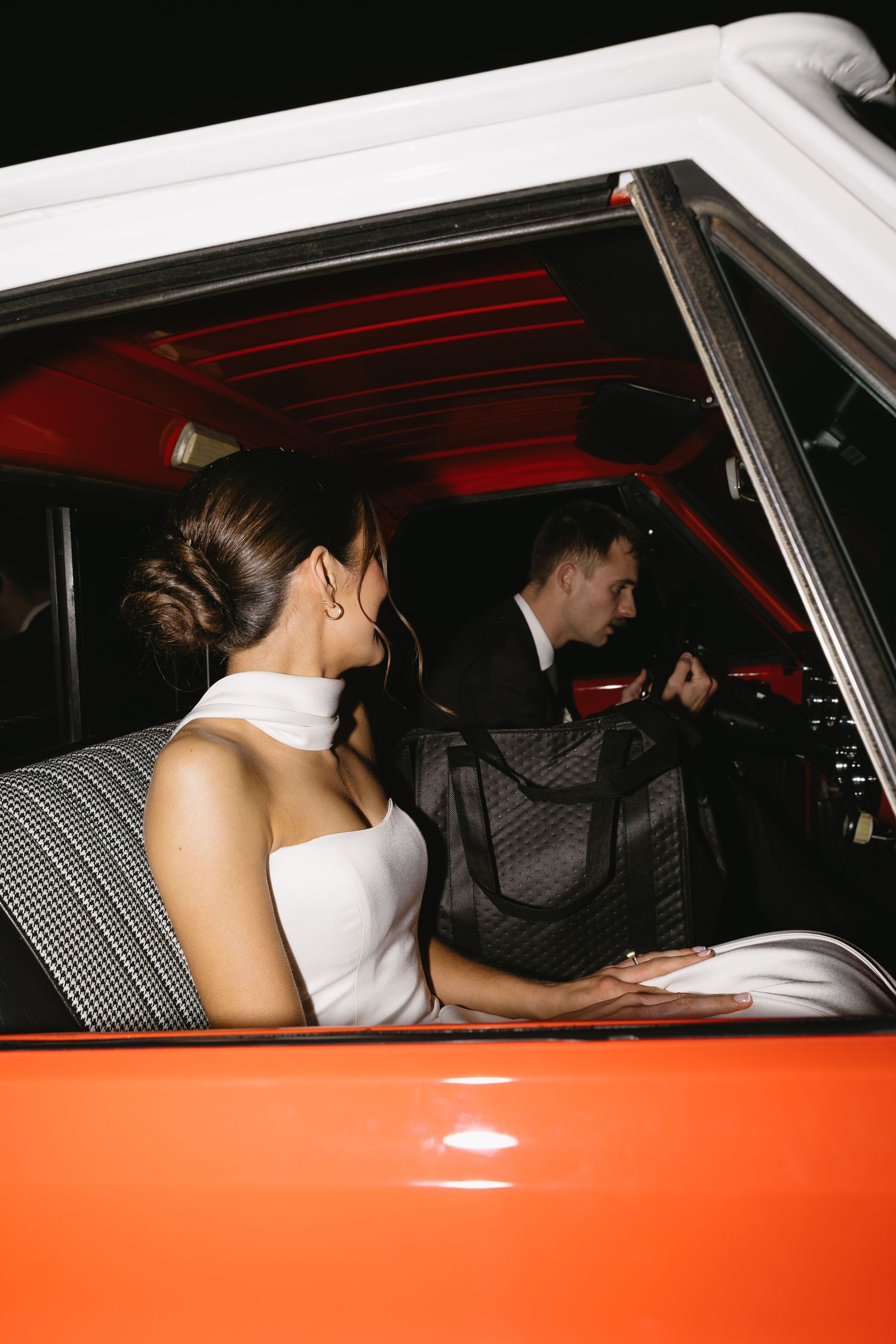 Newlyweds sitting in a vintage orange car after their wedding ceremony.