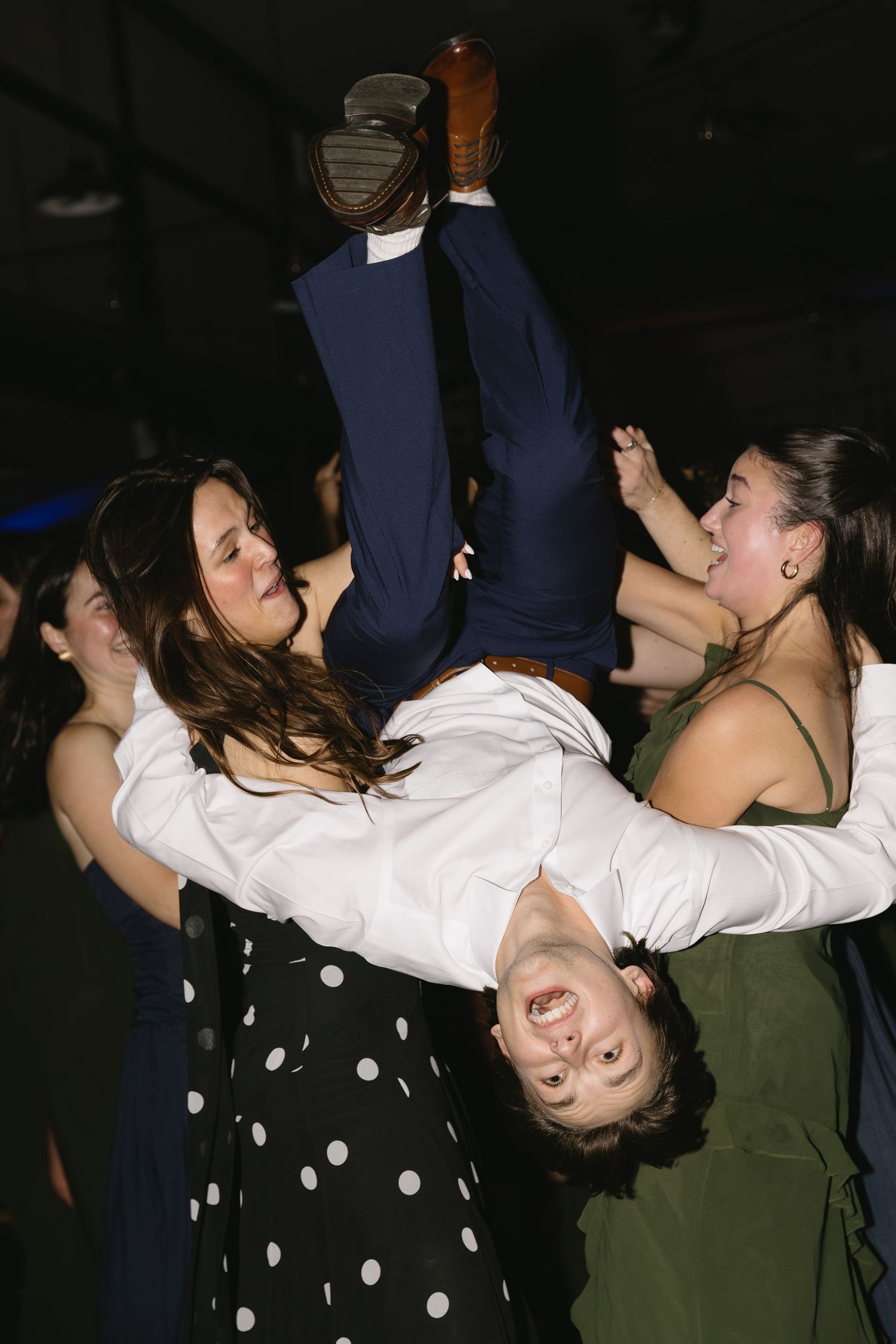 Wedding guests dancing energetically at a dimly lit reception party.