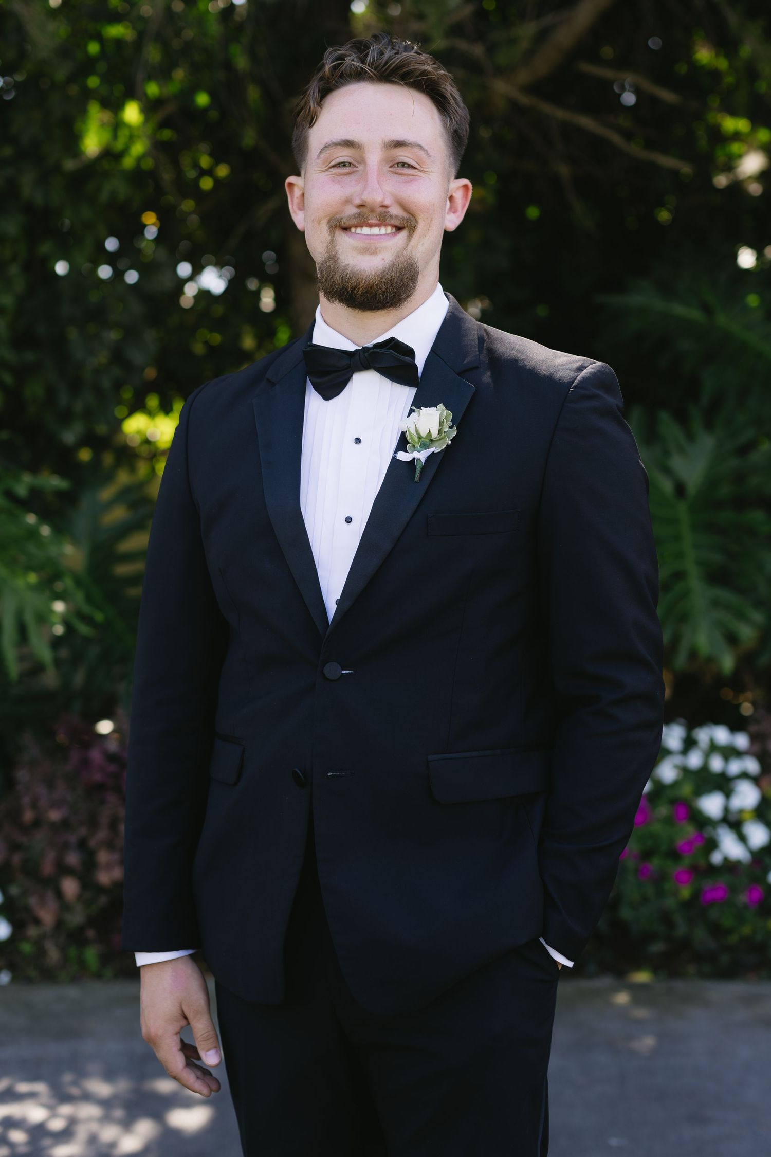 Groom in classic black tuxedo and bowtie smiles in outdoor wedding portraits.