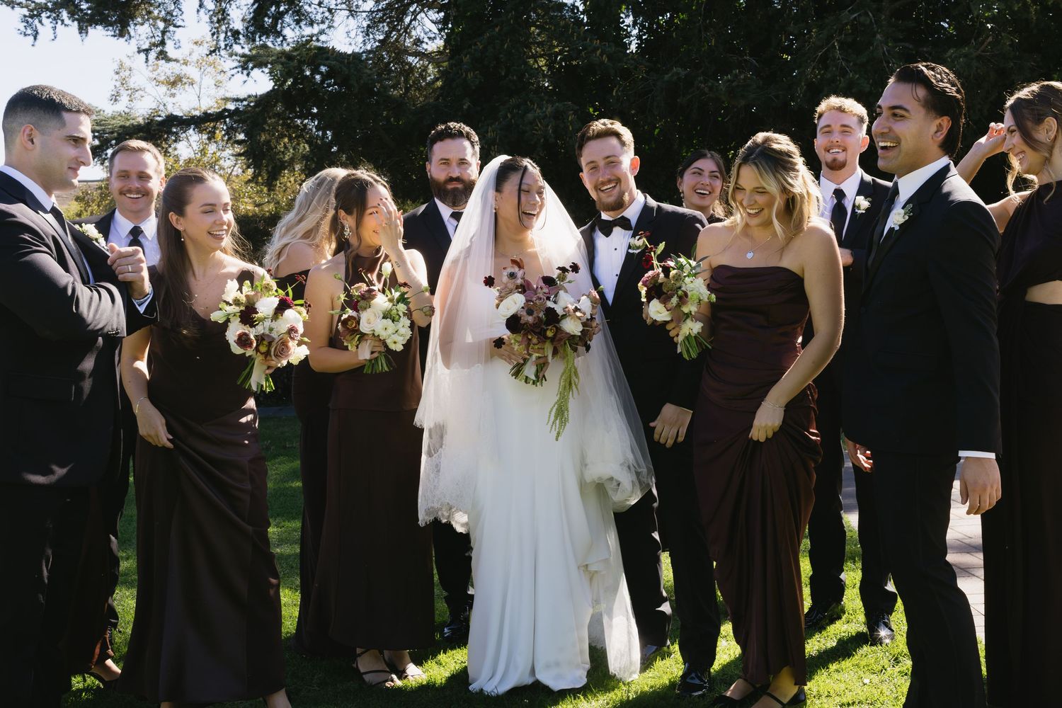Wedding party celebrating outdoors with joyful expressions in formal attire.