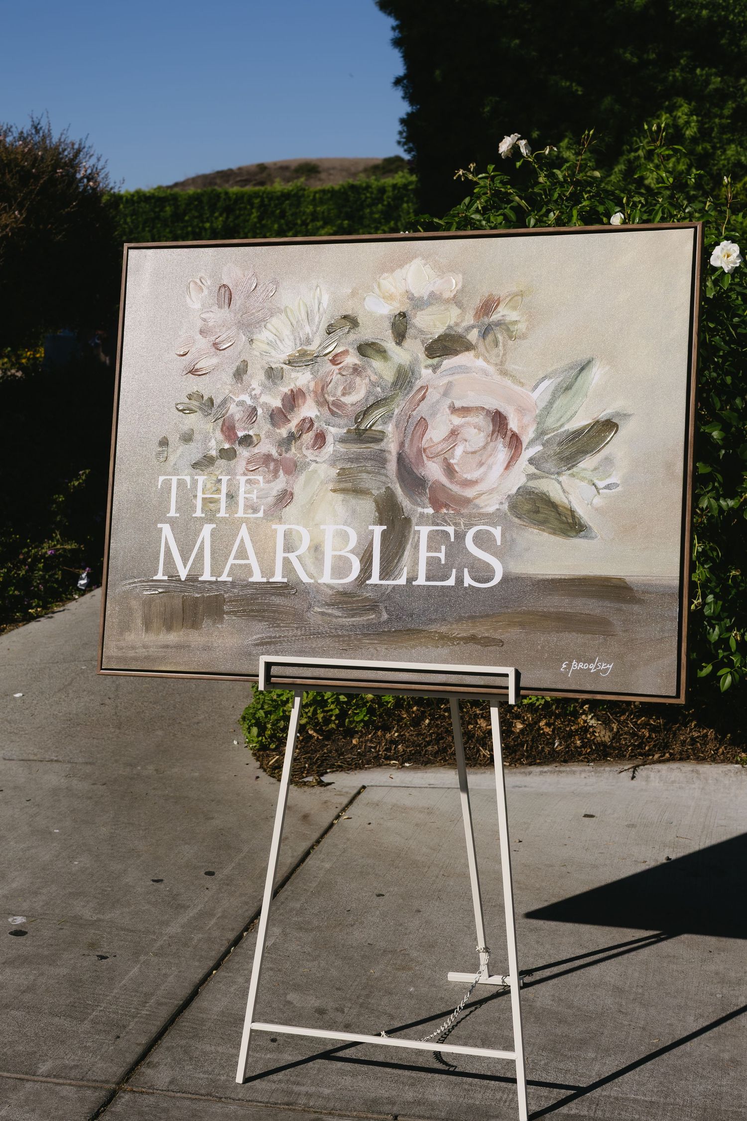 Elegant wedding sign reading 'The Mardles' decorated with painted roses on display at outdoor venue.