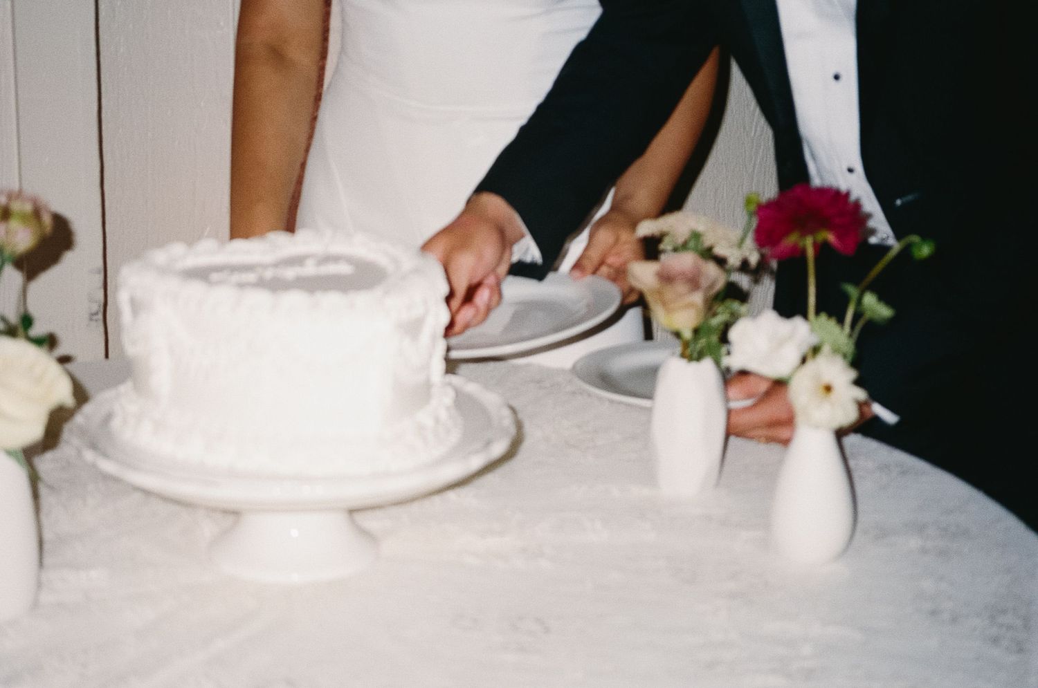 A row of wedding guests cutting into individual slices of white wedding cake at an elegant reception.
