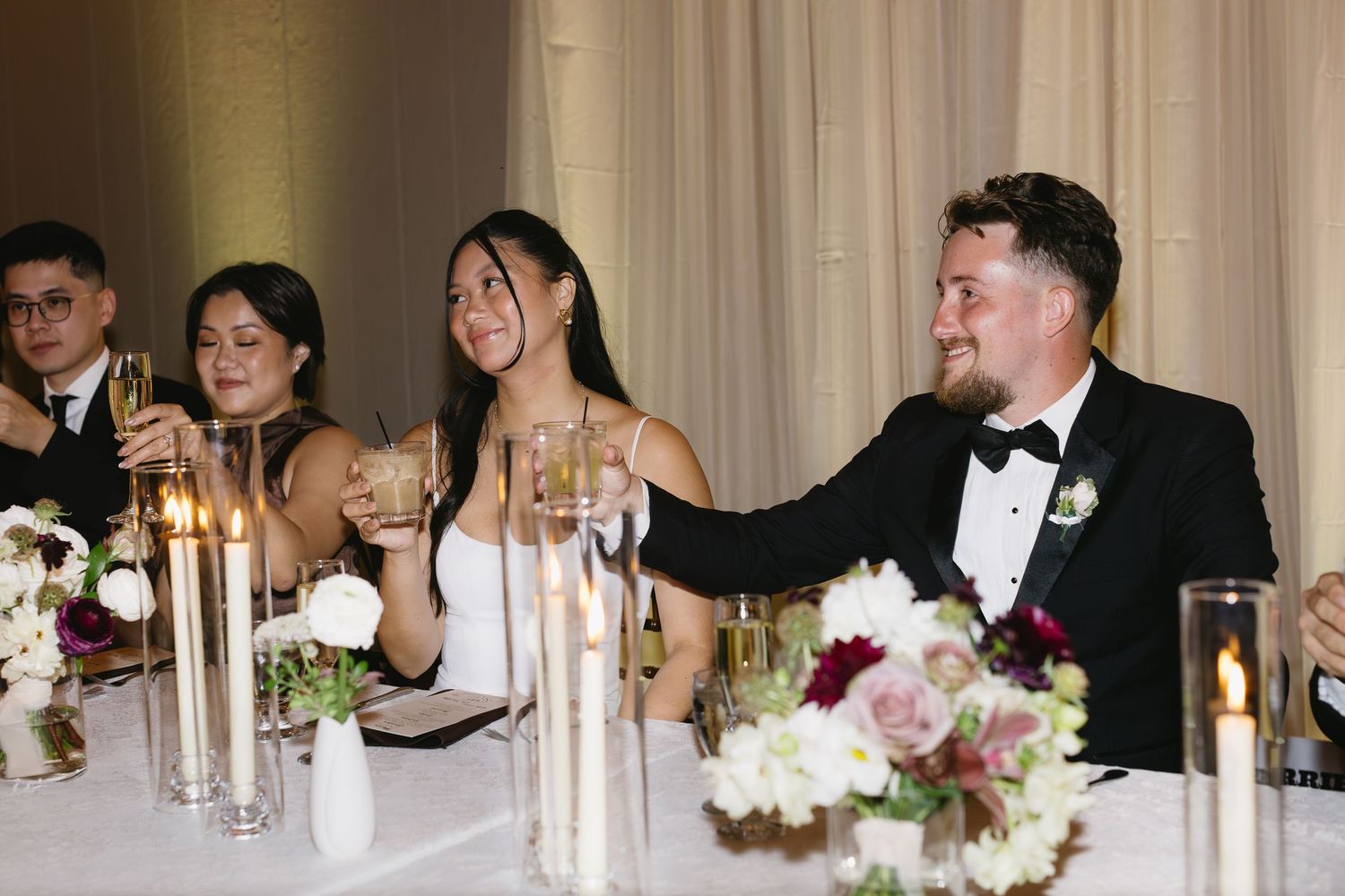 Wedding reception dinner scene with elegant table settings and white floral centerpieces.