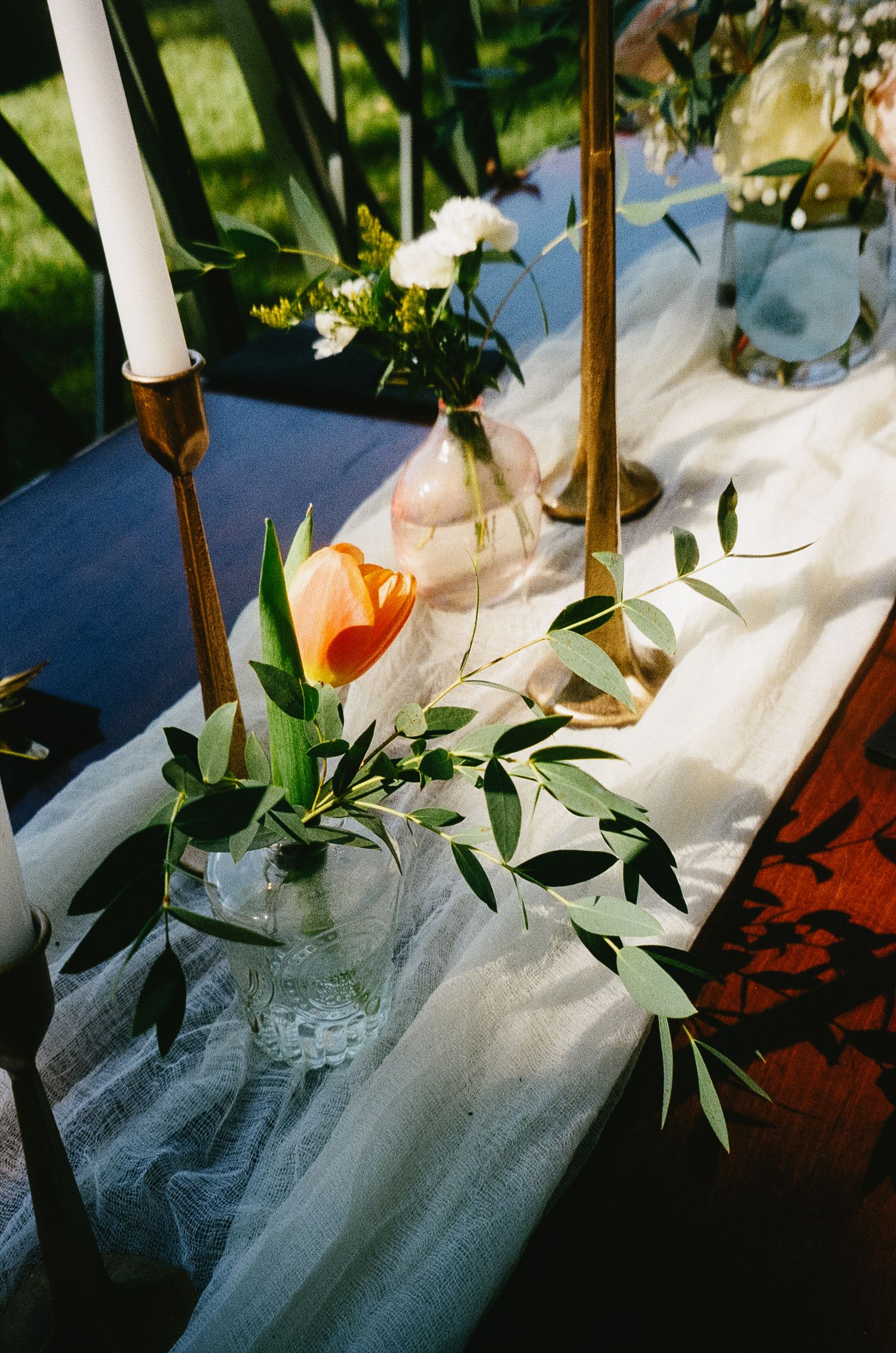 Elegant wedding table decor with white tulle fabric, greenery, and glass candle holders in a romantic garden setting.