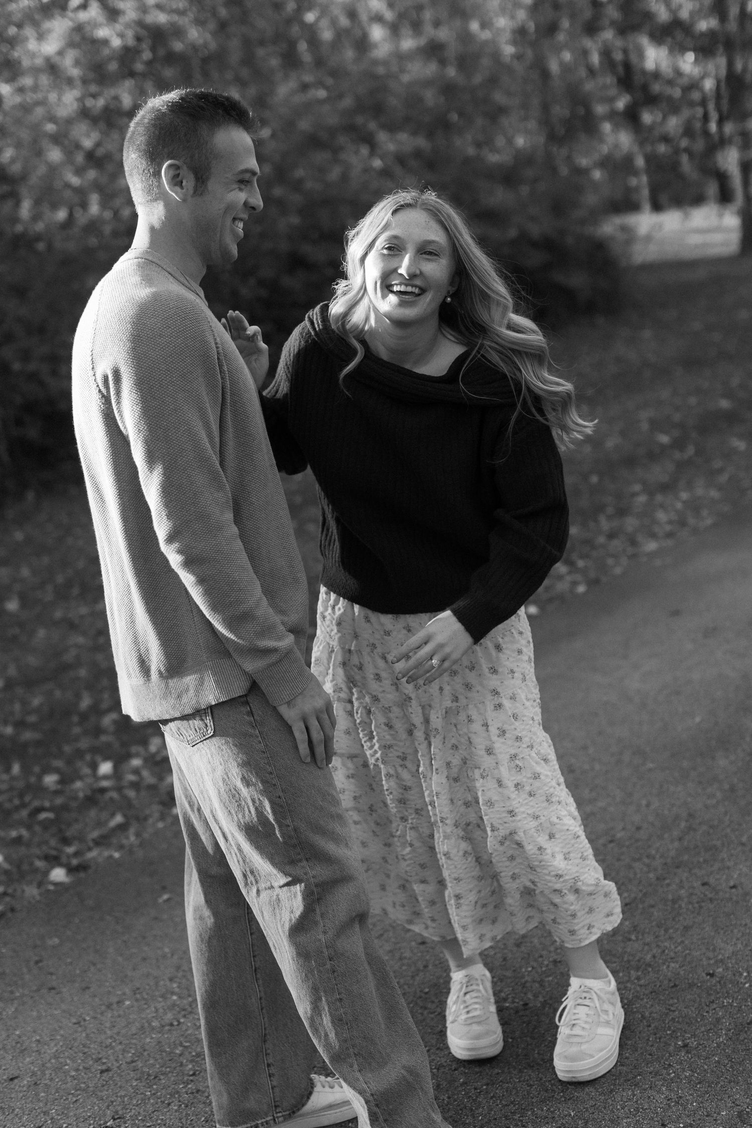 Candid black and white shots of a couple laughing together on a park path.