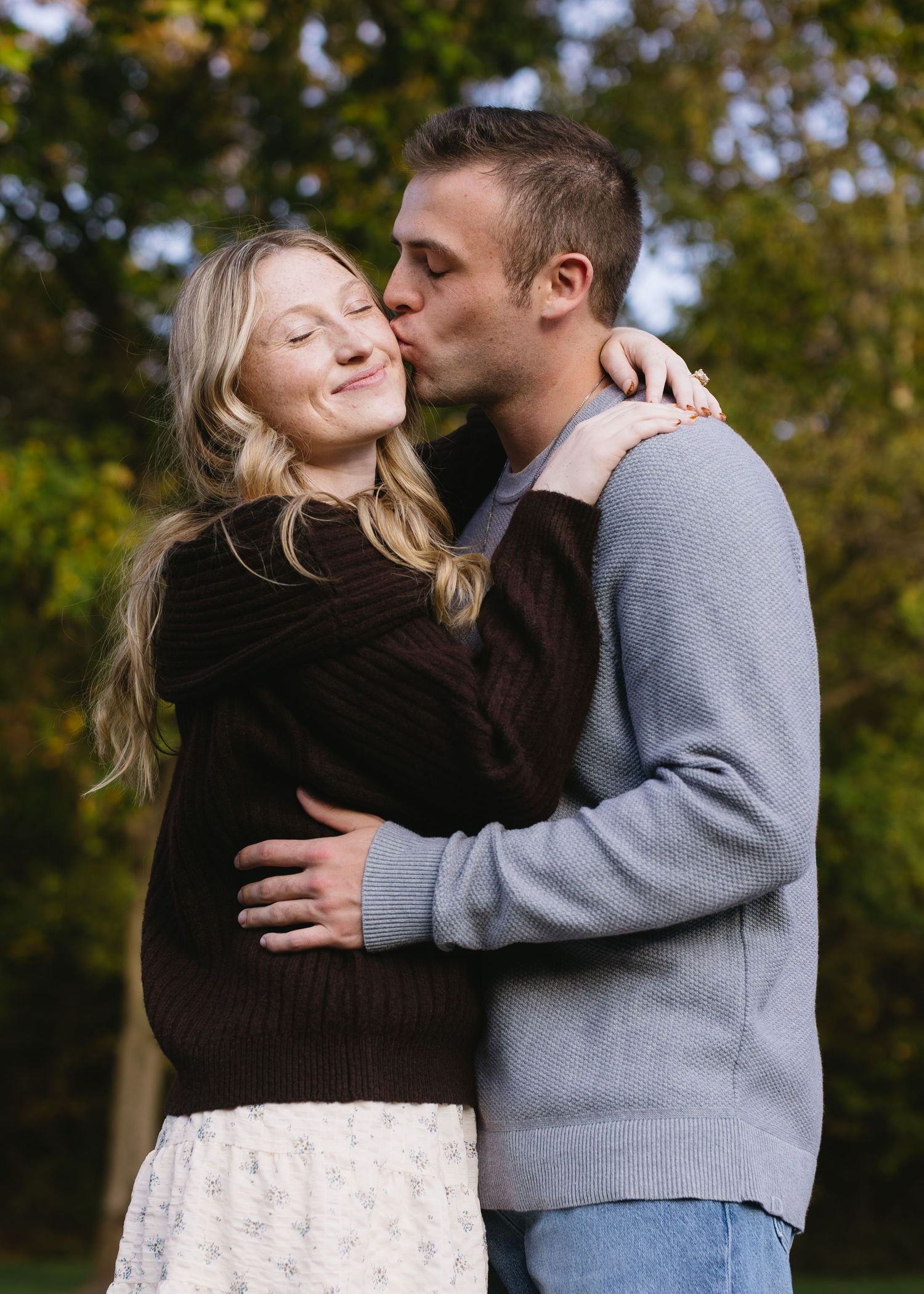 Romantic couple embraces in warm sunlight against autumn foliage background.