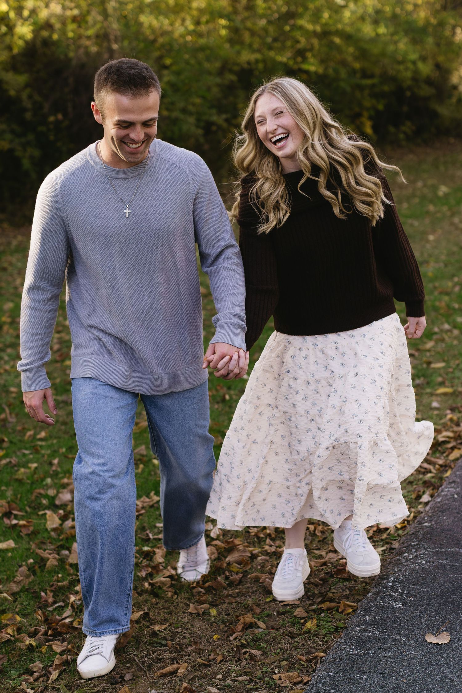 Couple walking together on autumn path with fallen leaves, wearing casual clothes and holding hands.