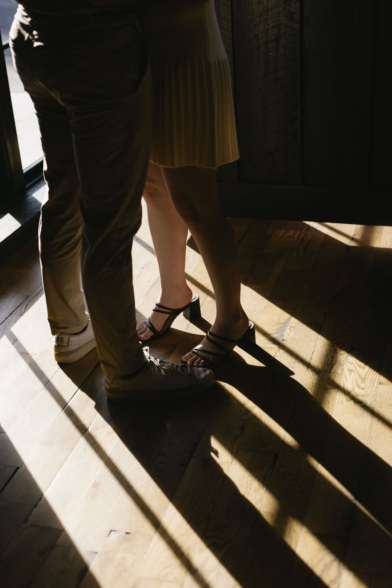 Dramatic shadows cast on floor showing feet and legs of people standing in a line with sunlight streaming in.