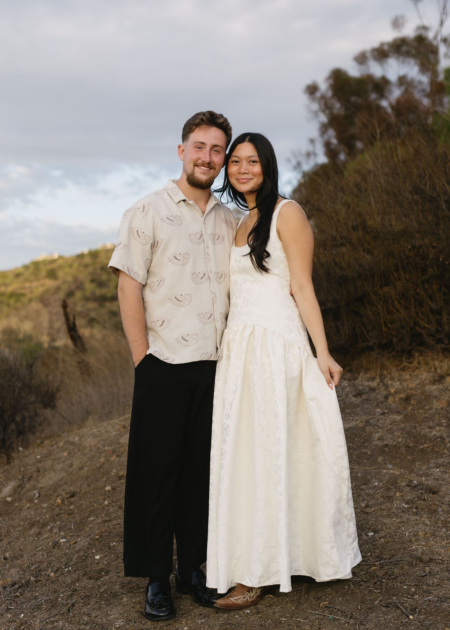 A couple poses for portraits on a rustic dirt path wearing coordinated casual outfits.