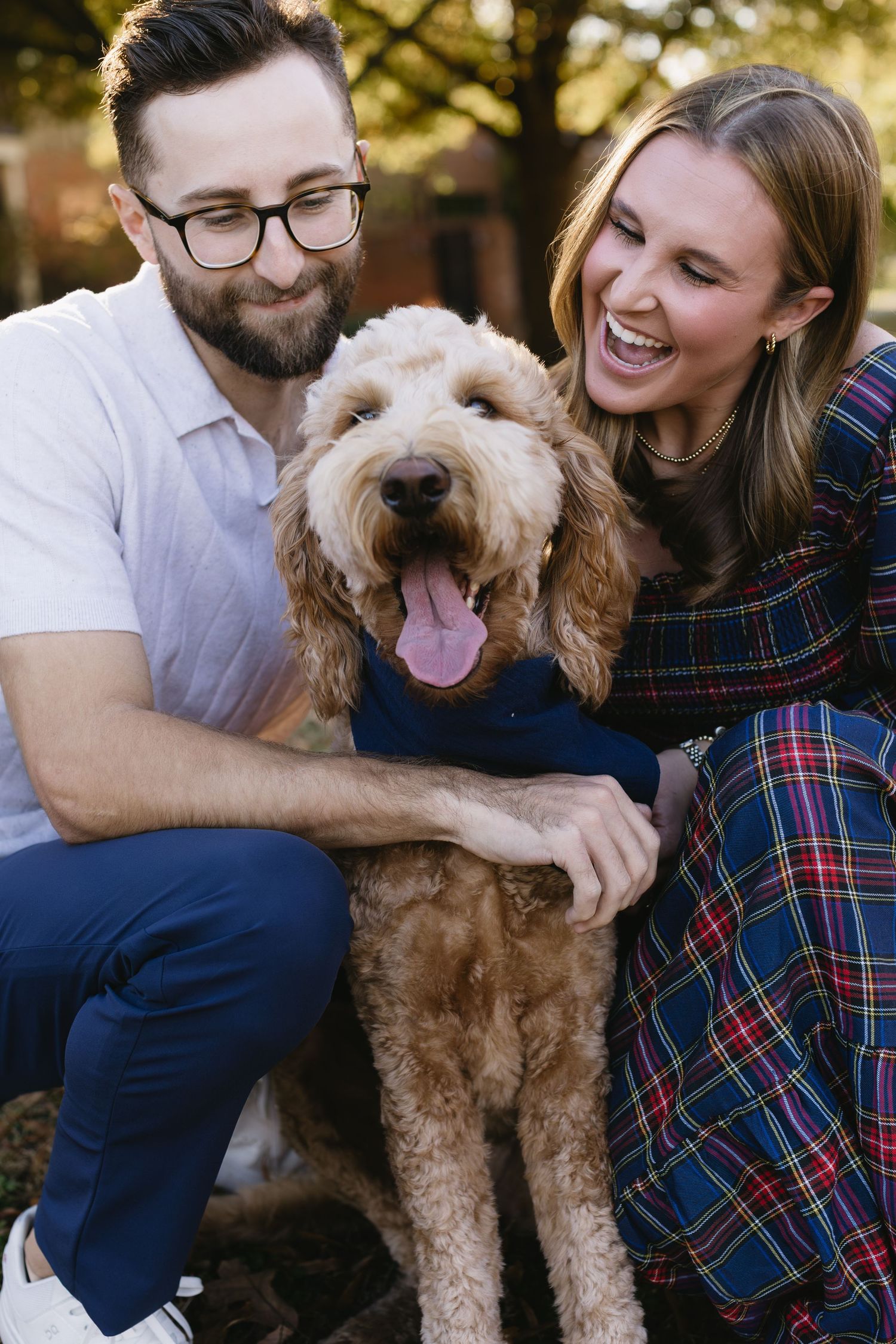 A couple and their happy Goldendoodle dog share a joyful moment together outdoors during golden hour.