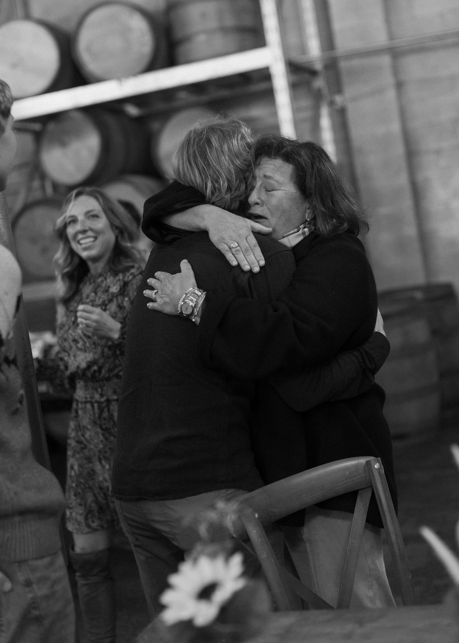 Black and white photo of people sharing emotional hugs at an event with wine barrels.