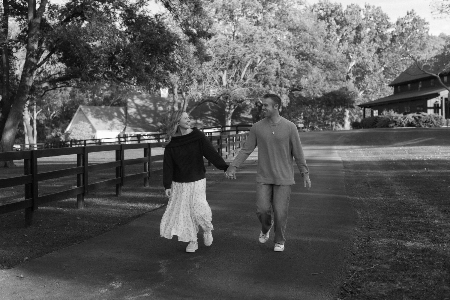 A couple walks hand in hand down a tree-lined path in a scenic park setting during autumn.
