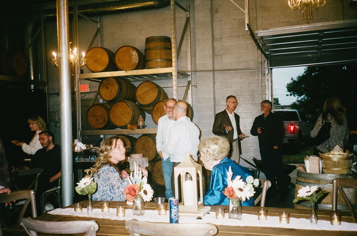 Reception venue interior with long tables and wine barrels visible in background lighting.
