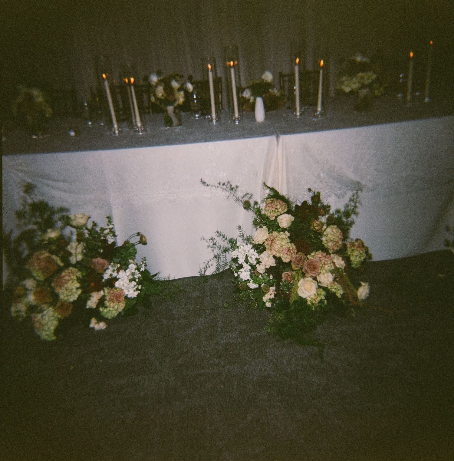 Low-light floral arrangements with pink and white blooms line a dark outdoor space creating an elegant garden ambiance.