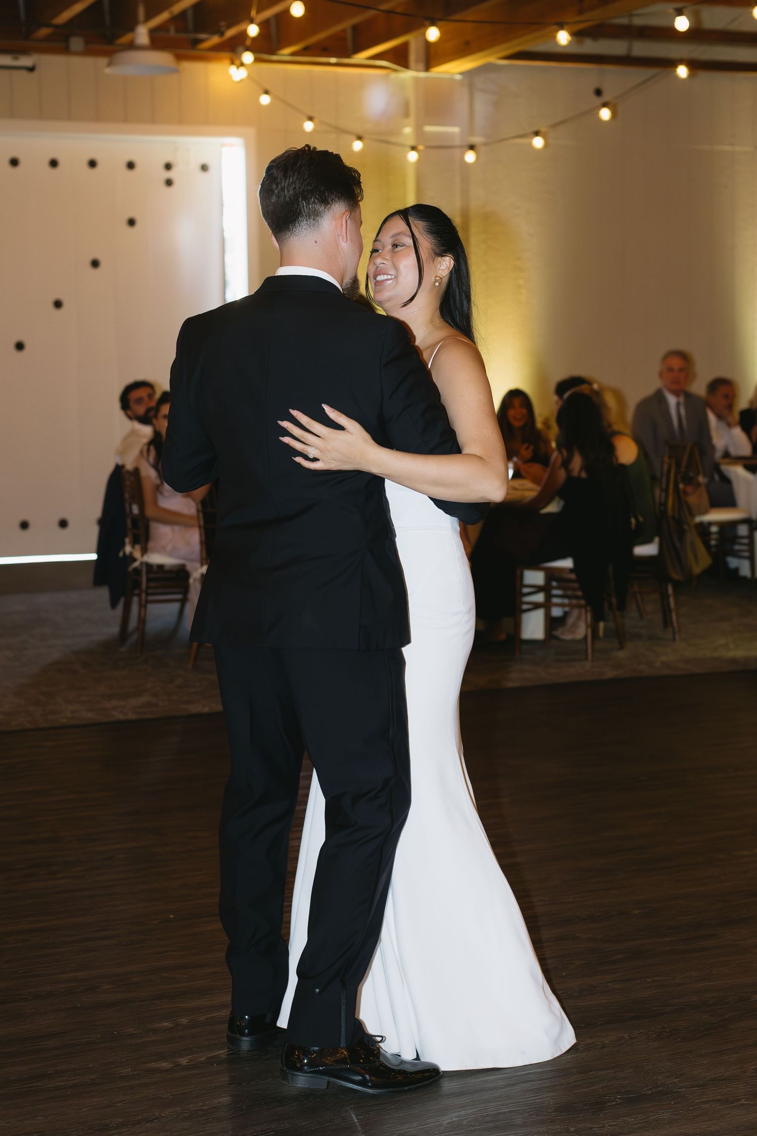 Couple shares their first dance in elegant reception venue with string lights overhead.