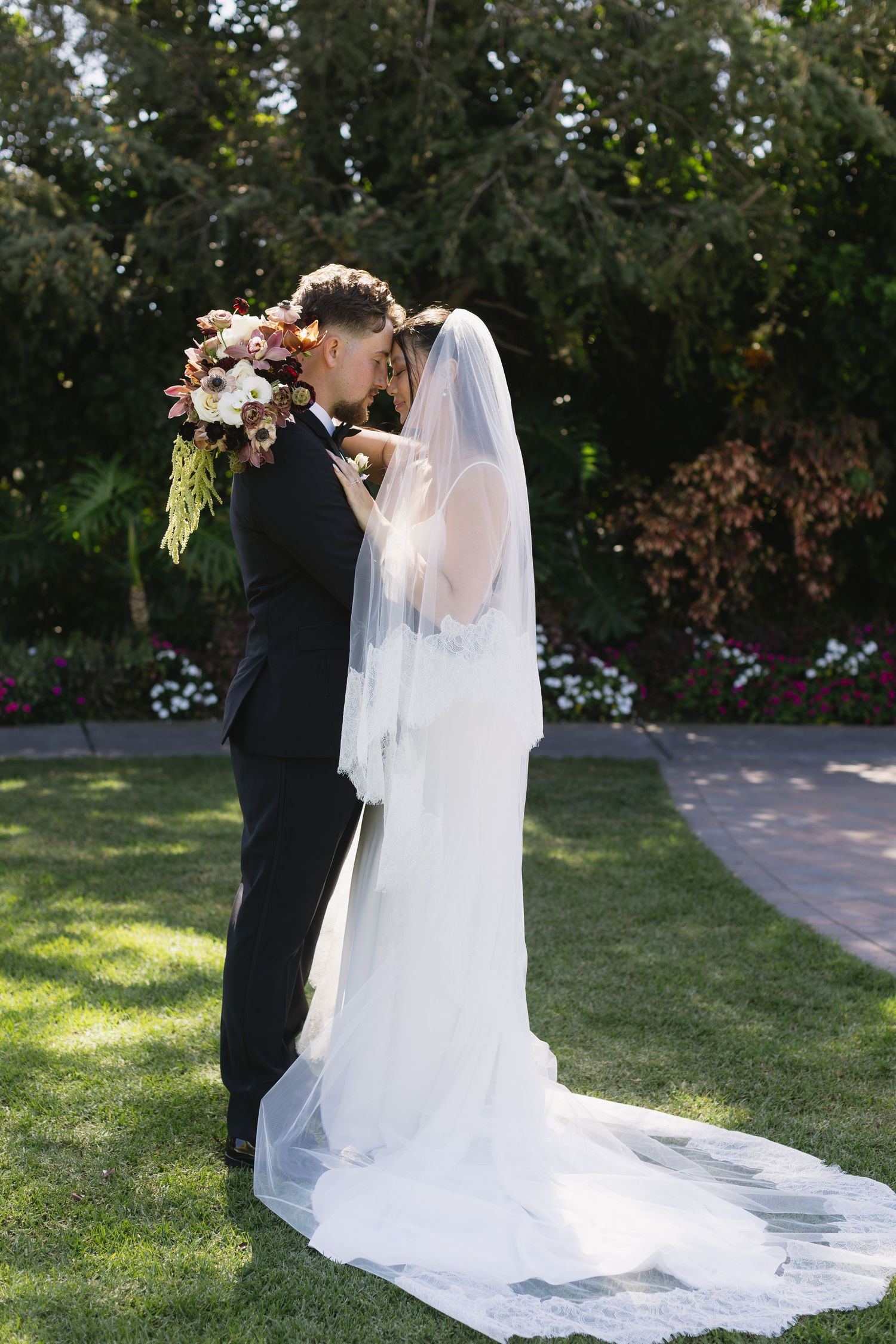Romantic outdoor wedding portraits with sunlit garden backdrop.