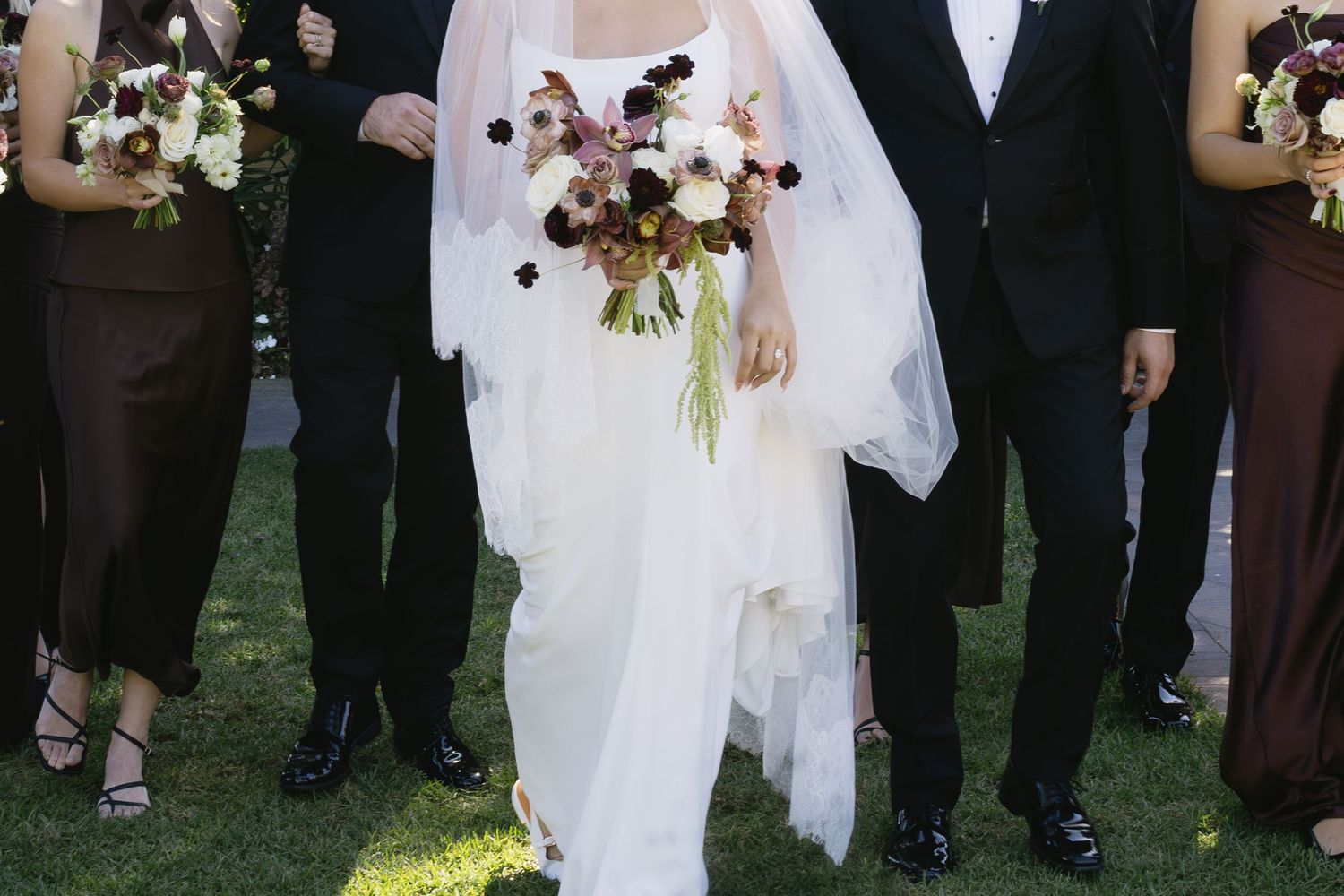 Close-up of a wedding party walking with burgundy and white floral bouquets.