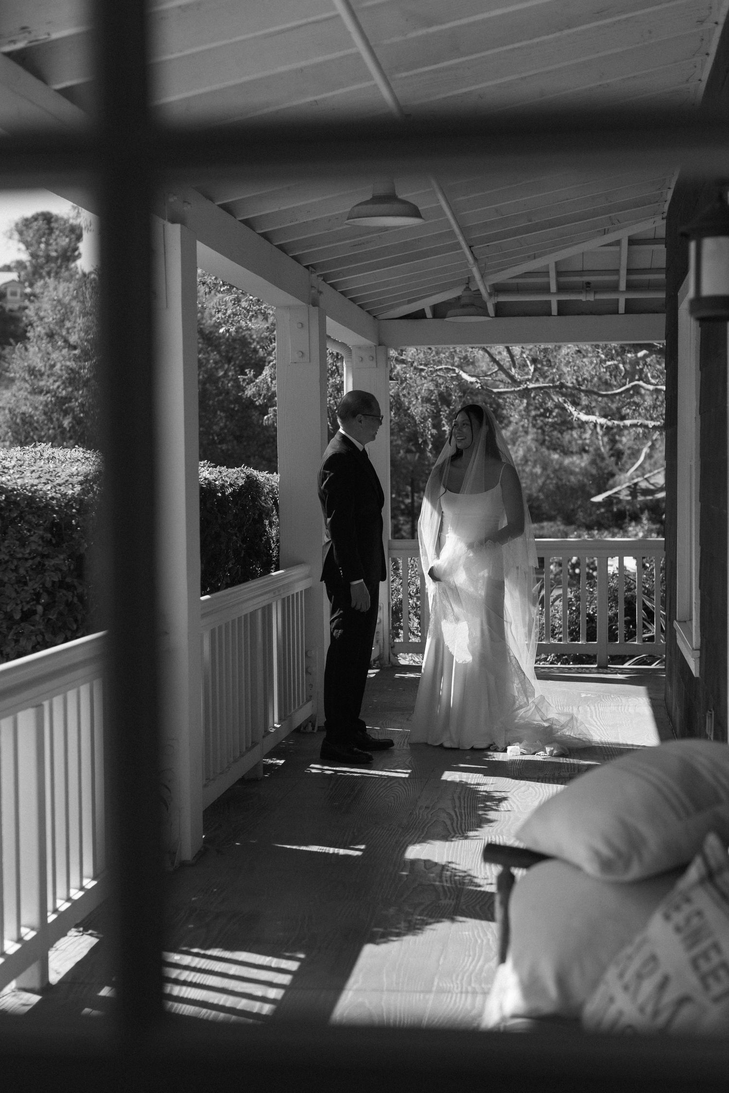 Black and white photo of a couple standing on a sunlit porch with white columns.