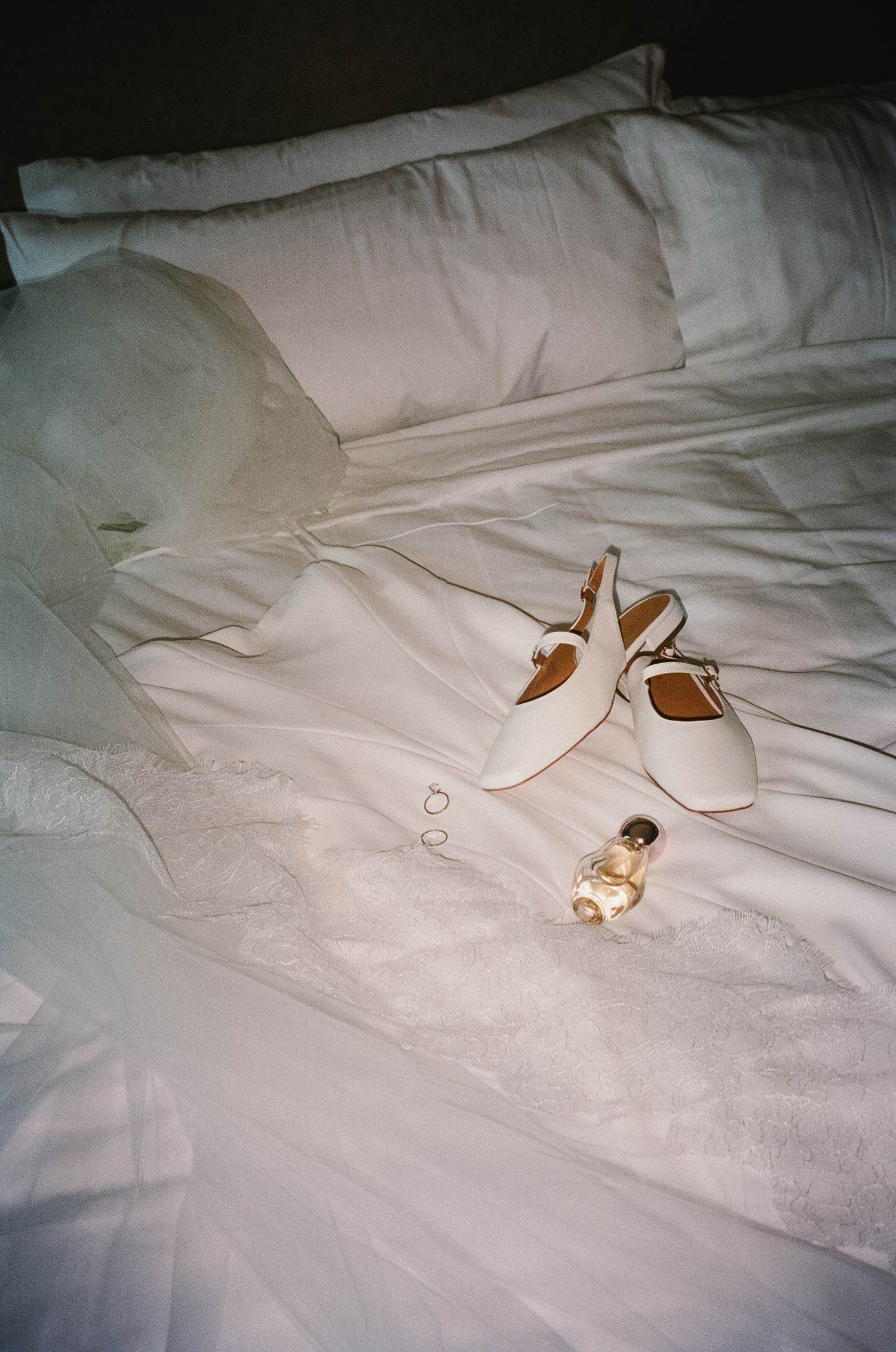 A pair of elegant white bridal shoes placed on crisp white bedding, photographed in natural light.