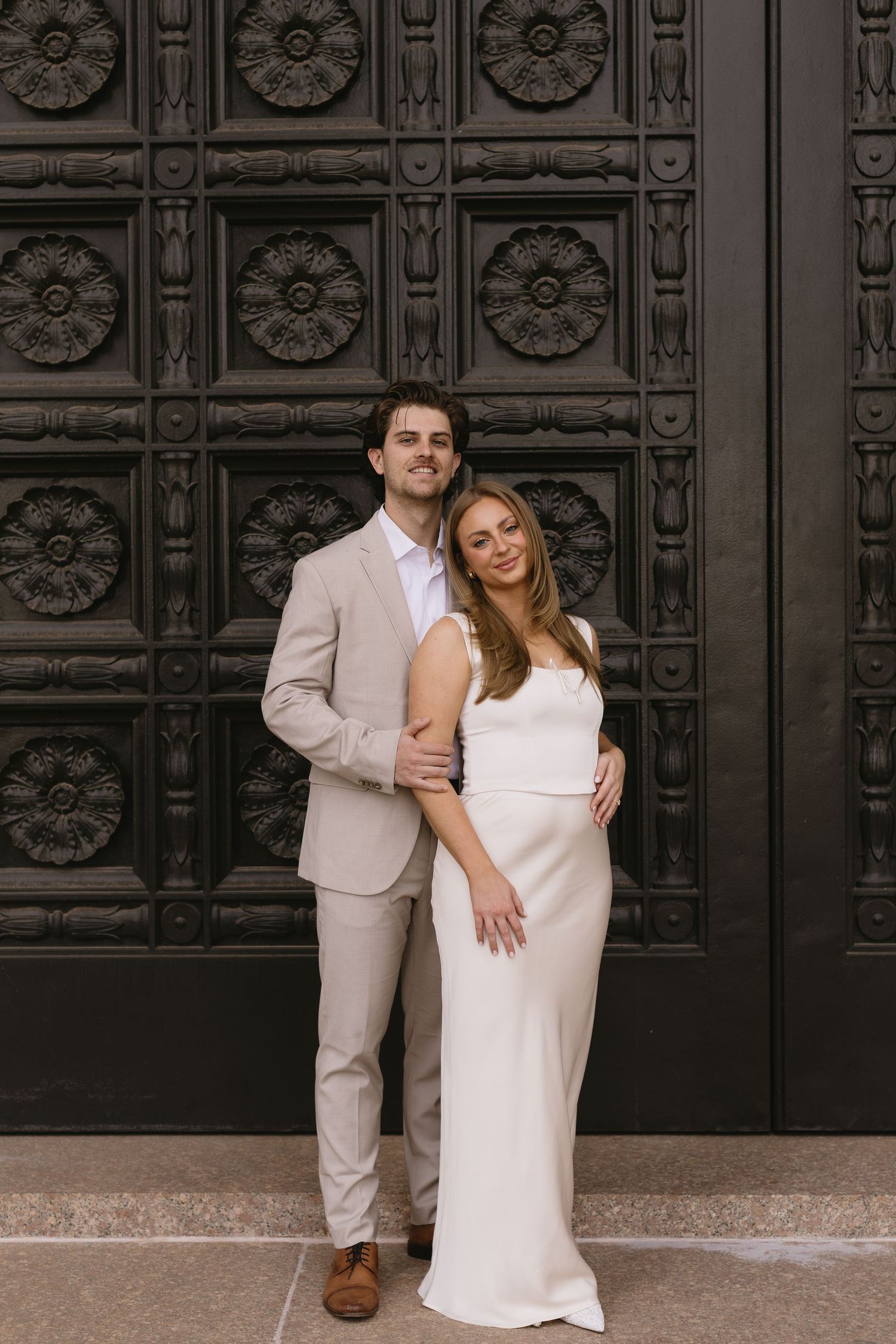 A couple poses against decorative dark doors in coordinated formal attire.