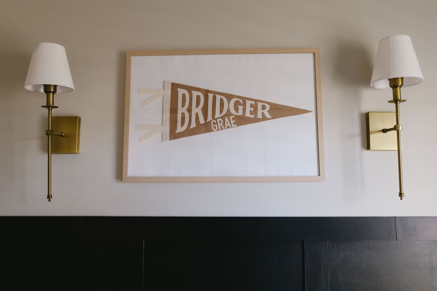 A vintage-style brown pennant design reading 'BRIDGER' mounted on a wall between two brass sconce lights.